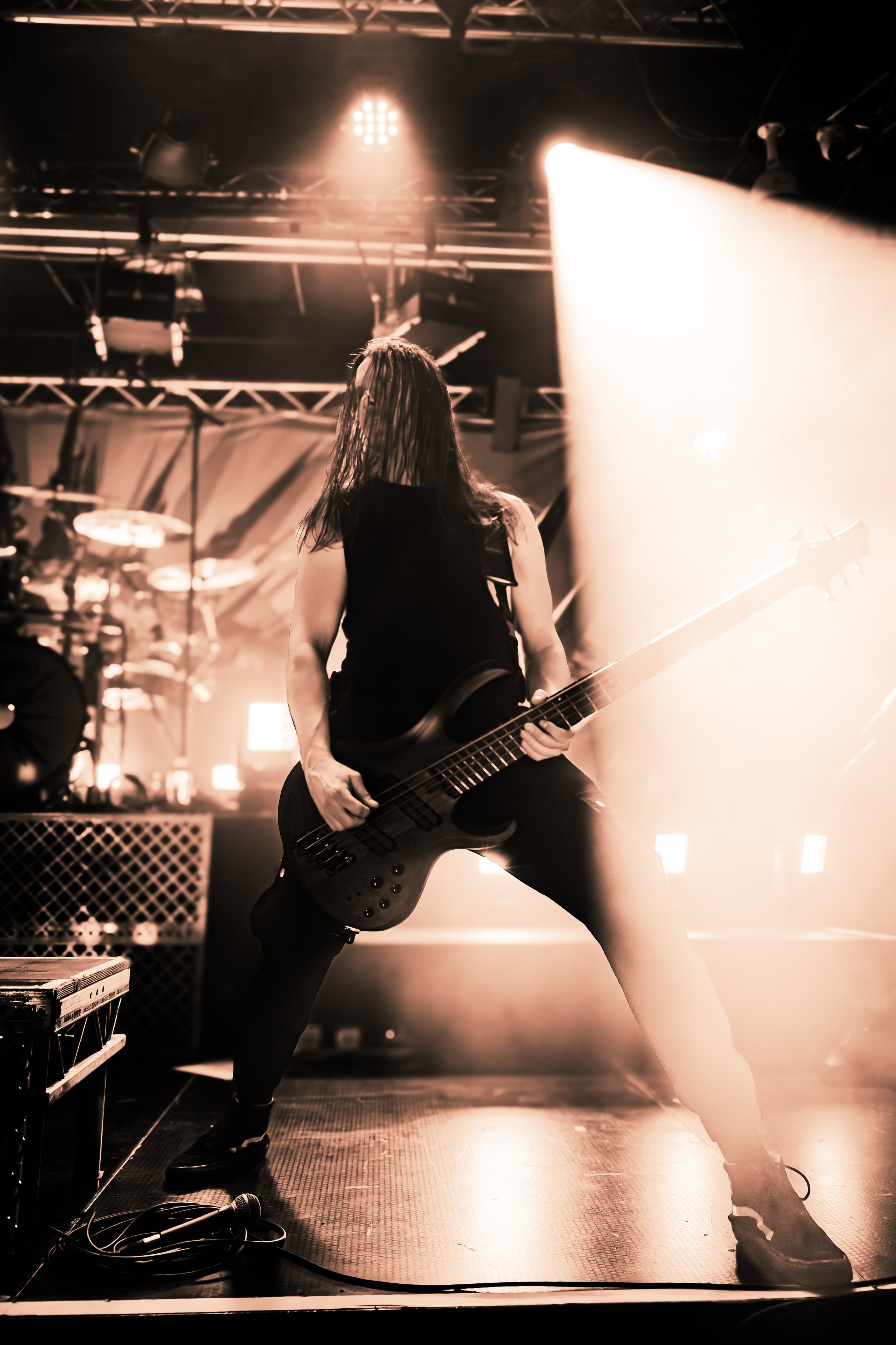 A guitarist with wet hair playing an electric guitar on stage during a concert, with stage lights and equipment around, captured in a dynamic pose.