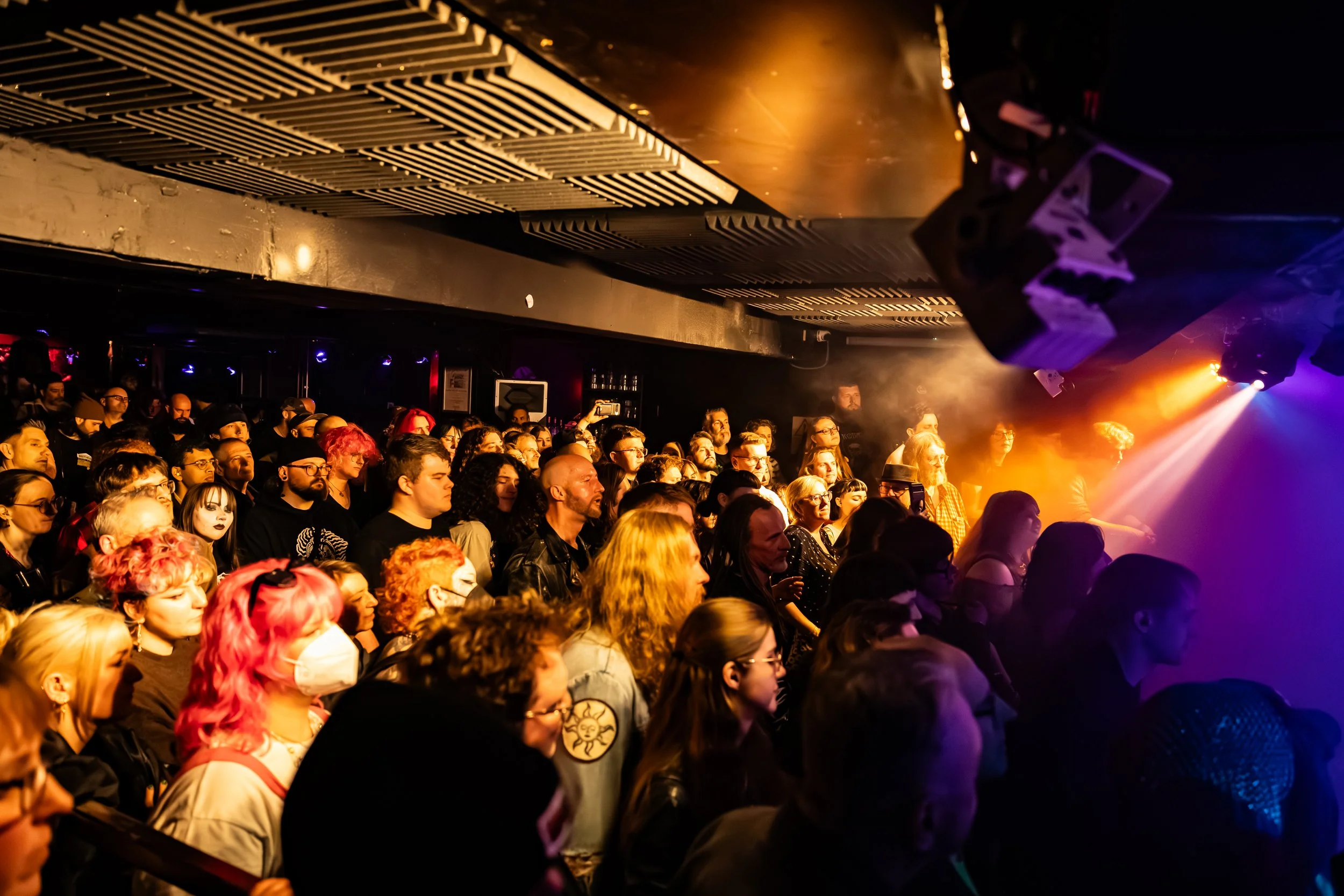 Crowd at concert or event with stage lighting and sound equipment.