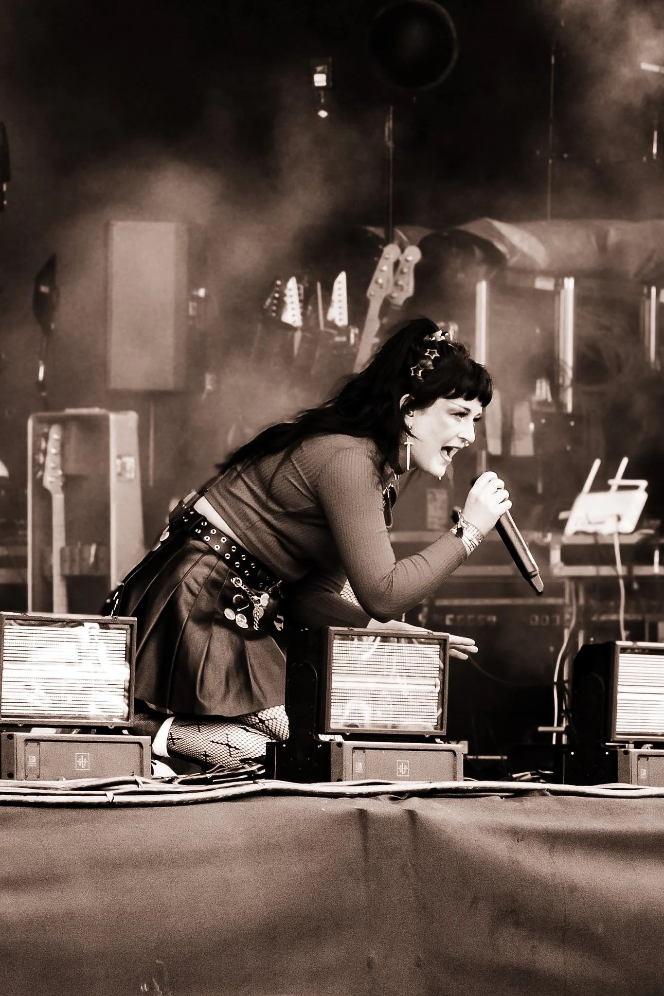 A woman singing into a microphone during a live performance, with stage equipment and speakers around her.
