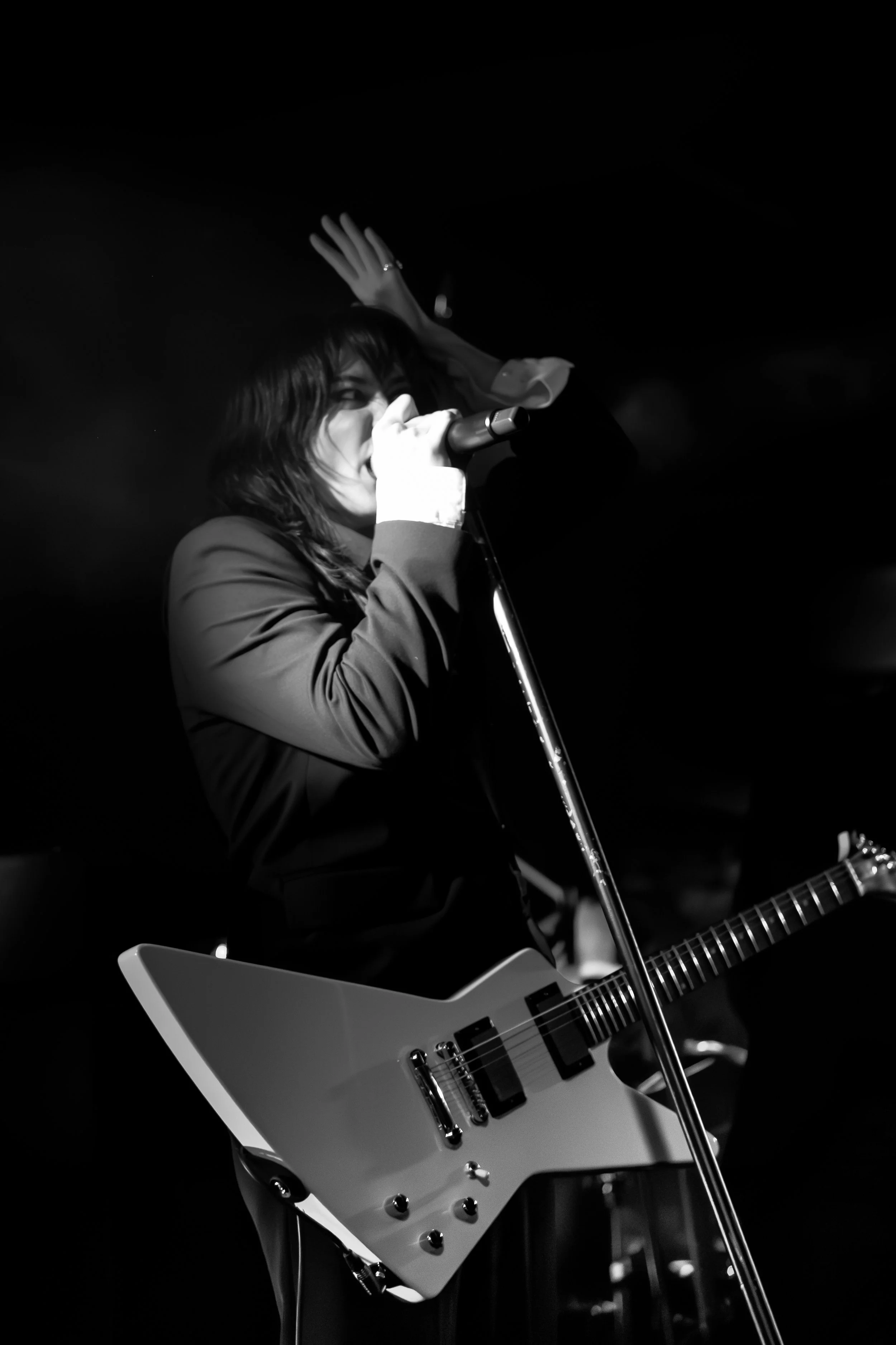 A woman singing into a microphone while playing a guitar on stage in black and white.