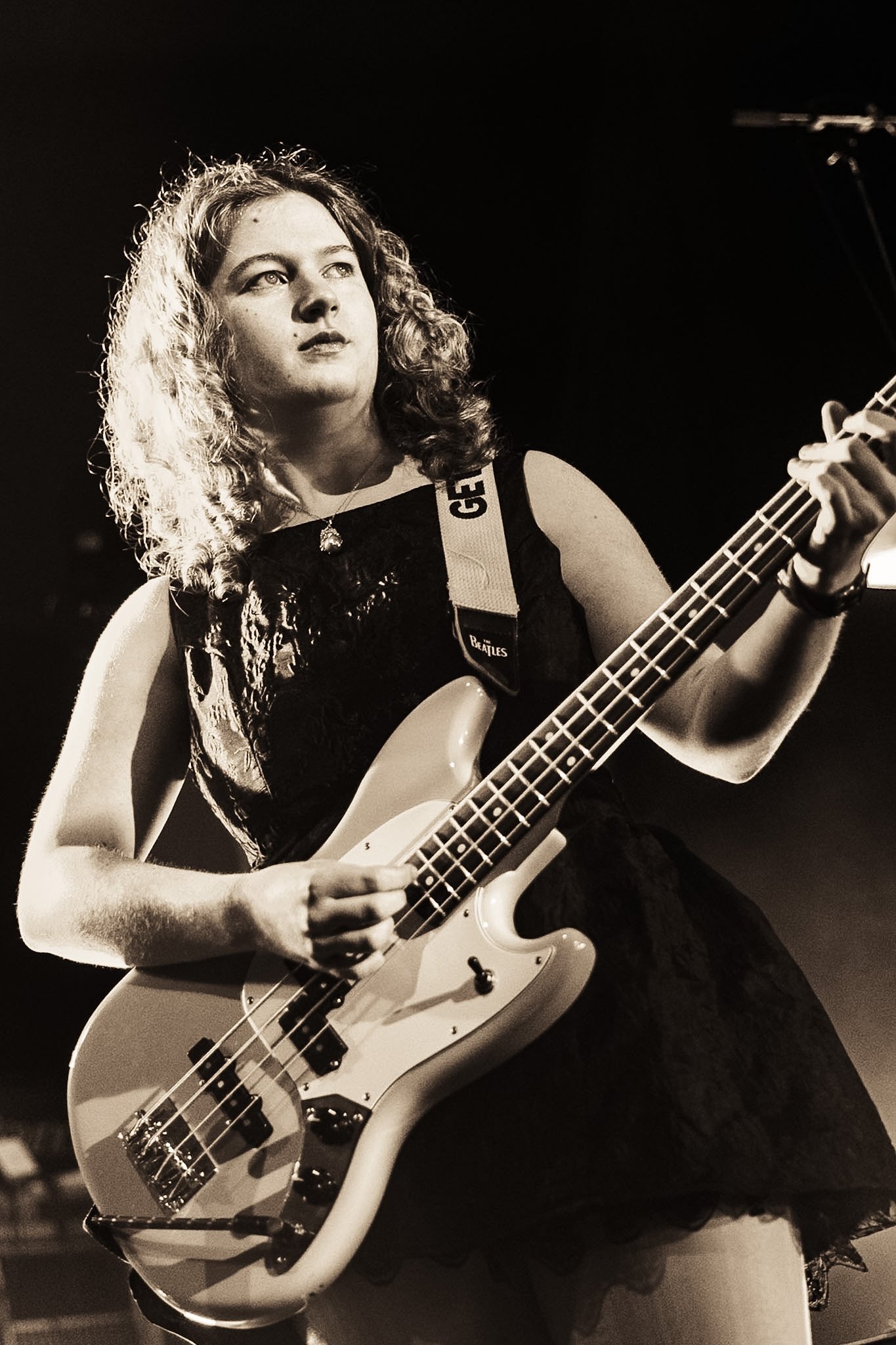 A woman with curly hair playing an electric bass guitar on stage.