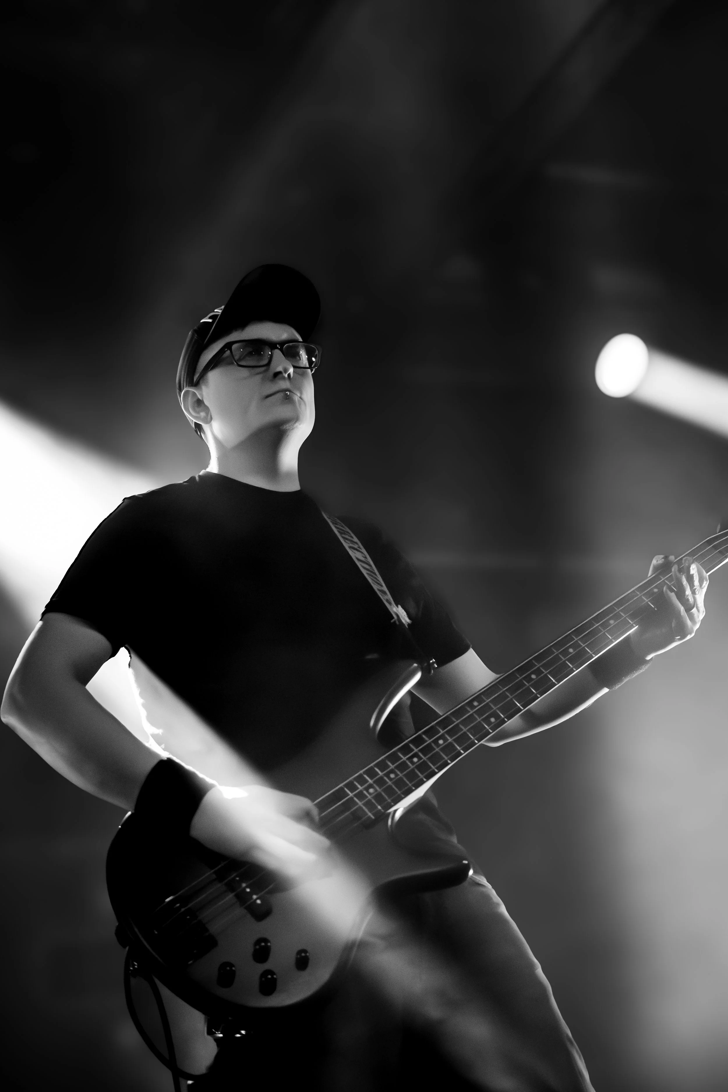 A person with glasses and a cap playing an electric guitar on stage in black and white.