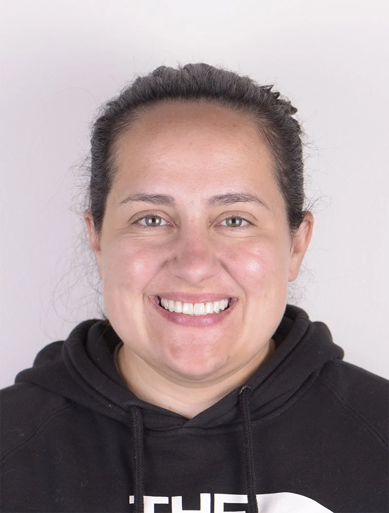 A woman smiling in front of a plain white background, wearing a black hoodie.
