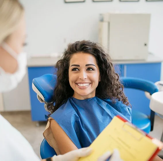 A young woman with curly hair smiling in a dental chair during a dental appointment.