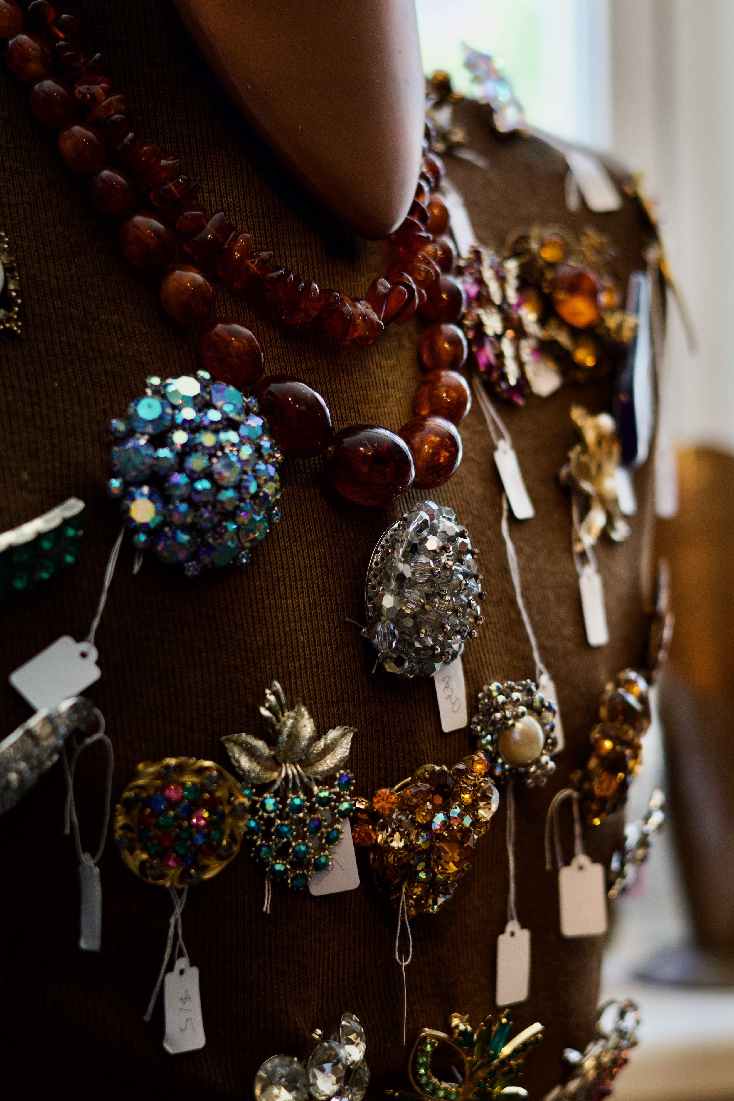 Close-up of various vintage brooches and jewelry displayed on a dark fabric background, with tags attached.