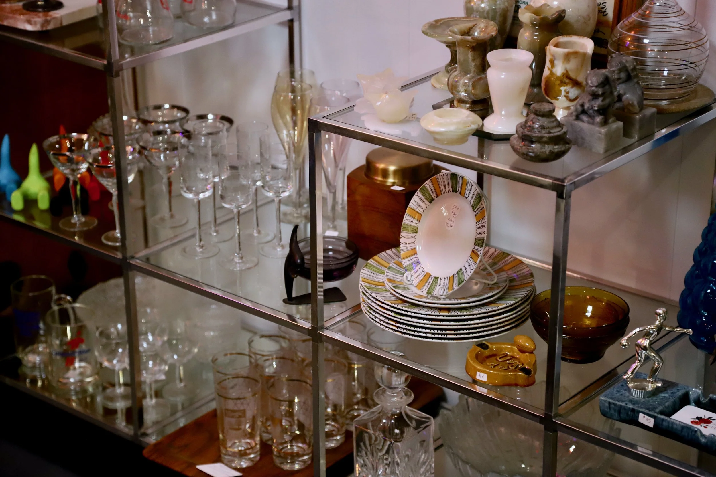 Display of various glass and ceramic vases and bowls on a multi-tiered shelving unit at an antique or thrift store.