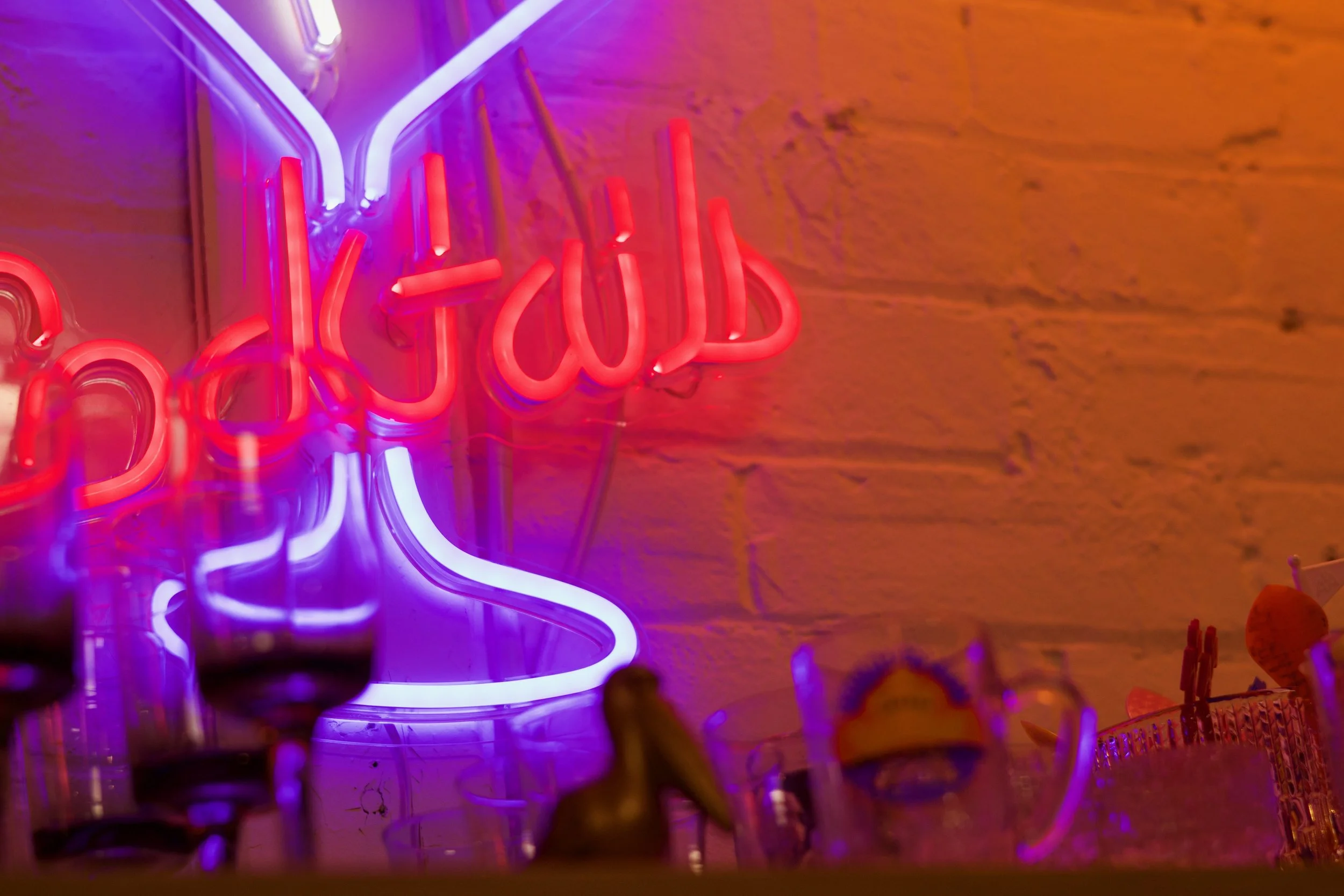 A neon cocktail sign with vintage MCM glassware below it.
