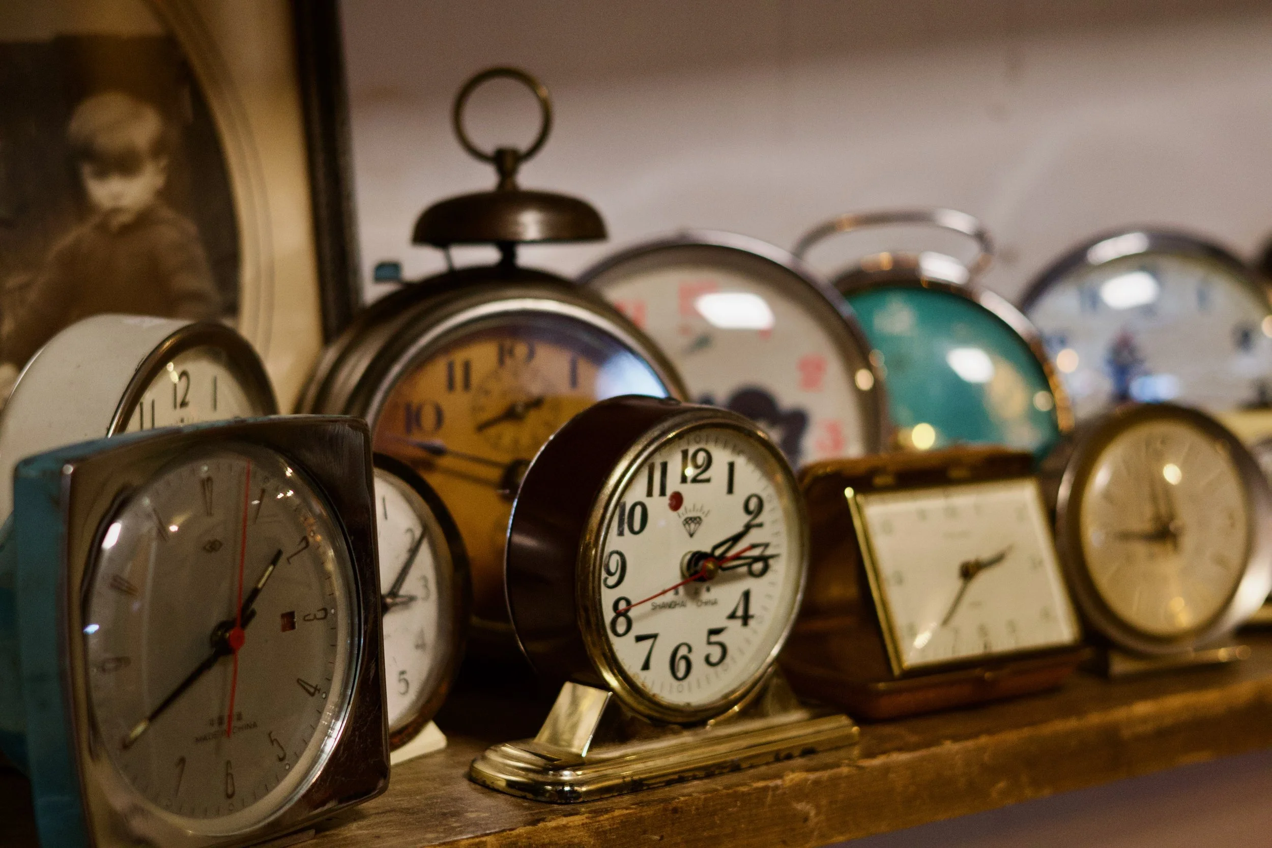 A collection of vintage analog clocks and alarm clocks arranged on a wooden surface, featuring various styles and colors.