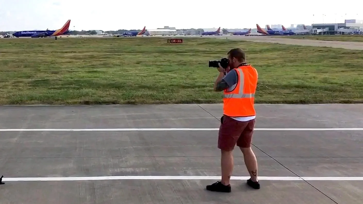 Ethan Avanzino operating a camera on an airport tarmac with Southwest Airlines planes in the background