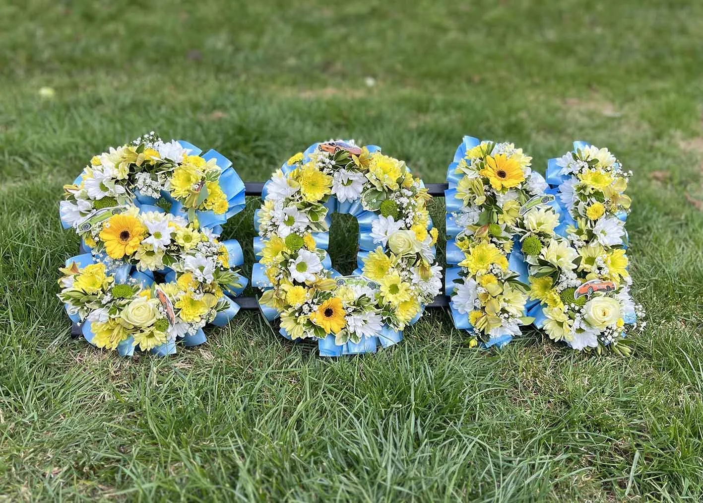 Floral arrangements spelling out '2021' with yellow, white, and green flowers on a grassy field.