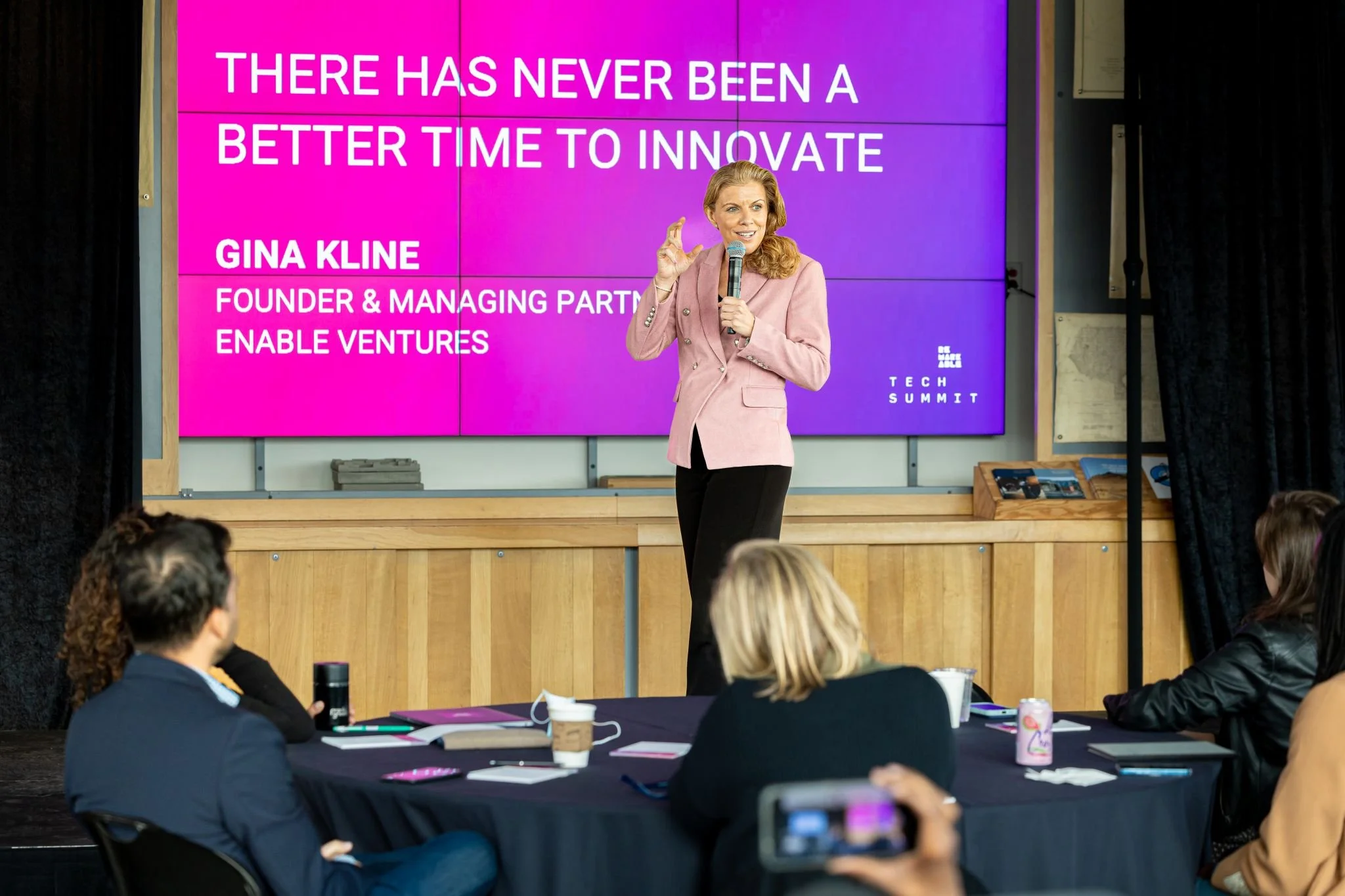 Gina Kline, SmartJob Founder and Managing Partner of Enable Ventures, speaks on stage at the Tech Summit. Behind her, a large screen displays the quote: "There has never been a better time to innovate."