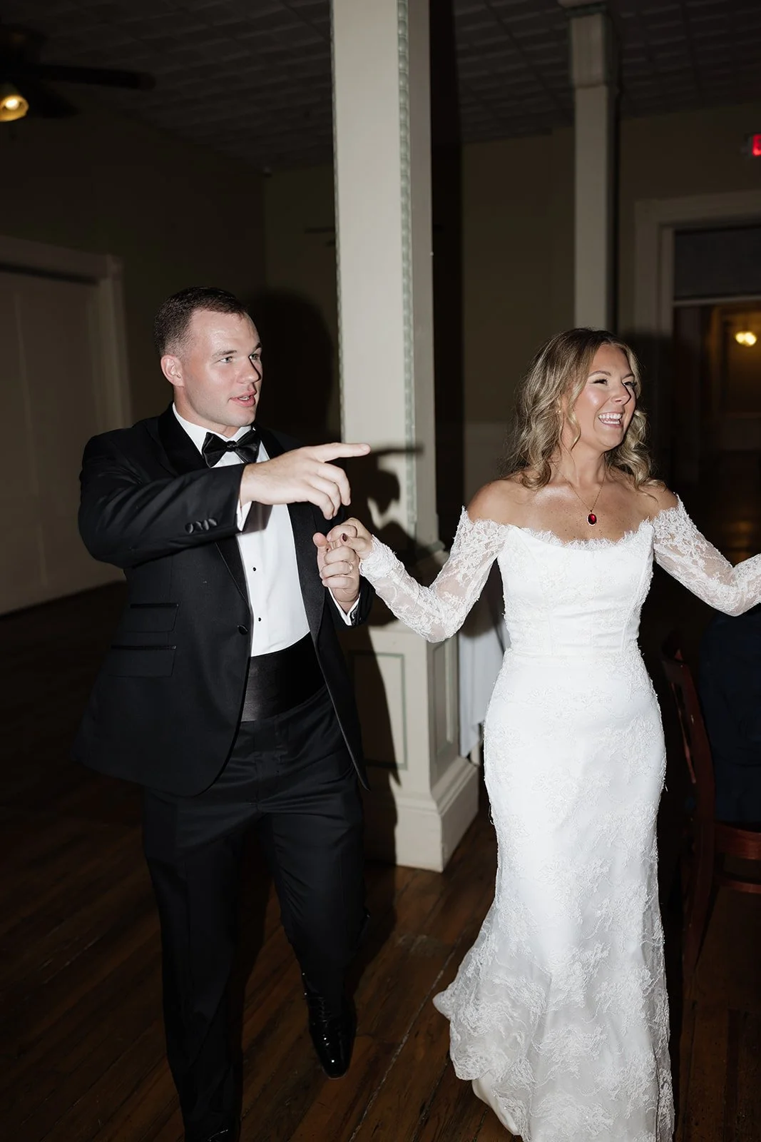 A bride and groom dancing at their wedding reception, the groom pointing and the bride smiling happily.