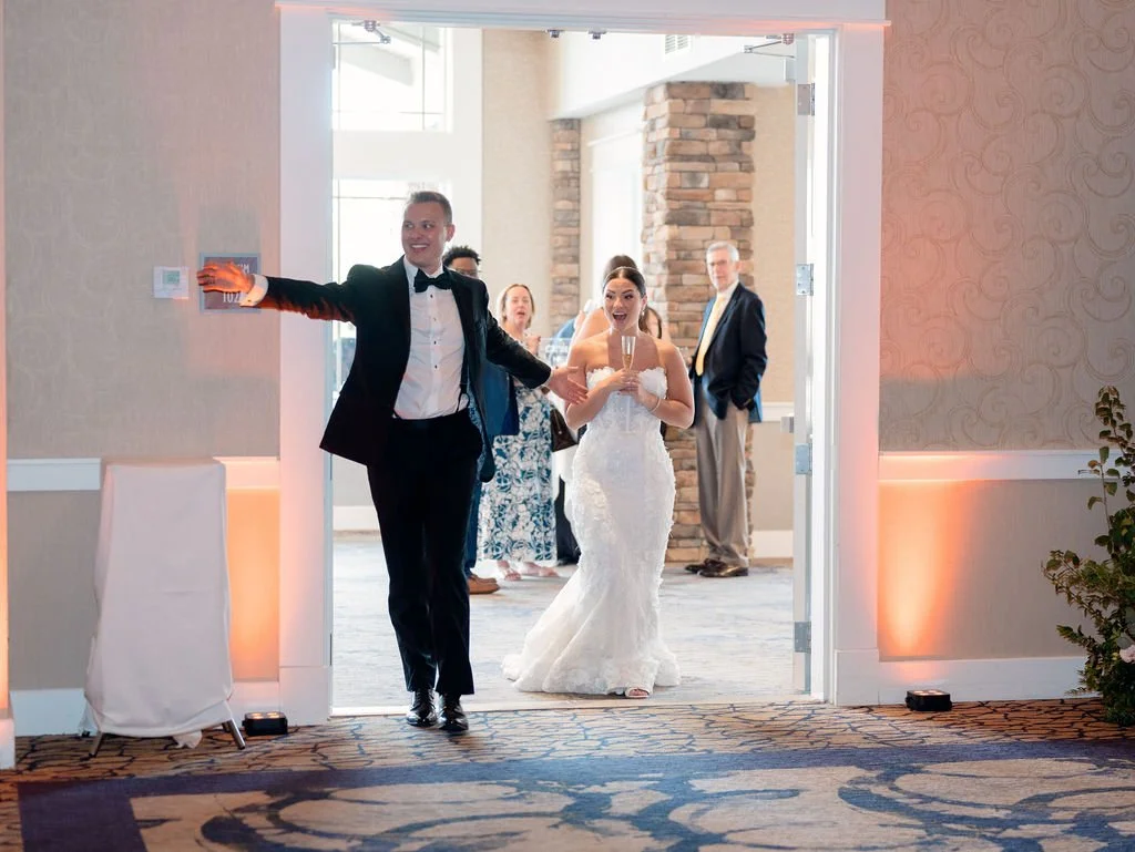Bride and groom entering reception, wedding celebration, guests in background, indoor venue with brick accents.