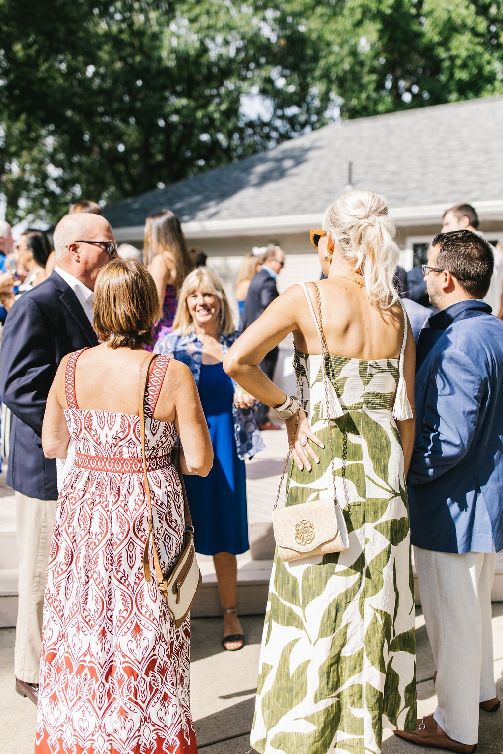 People socializing at an outdoor gathering on a sunny day, dressed in summer attire.