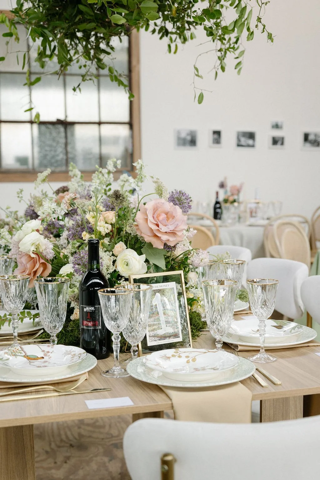 Elegant dinner table setup with a floral centerpiece, wine bottles, and crystal glassware in a decorated room.