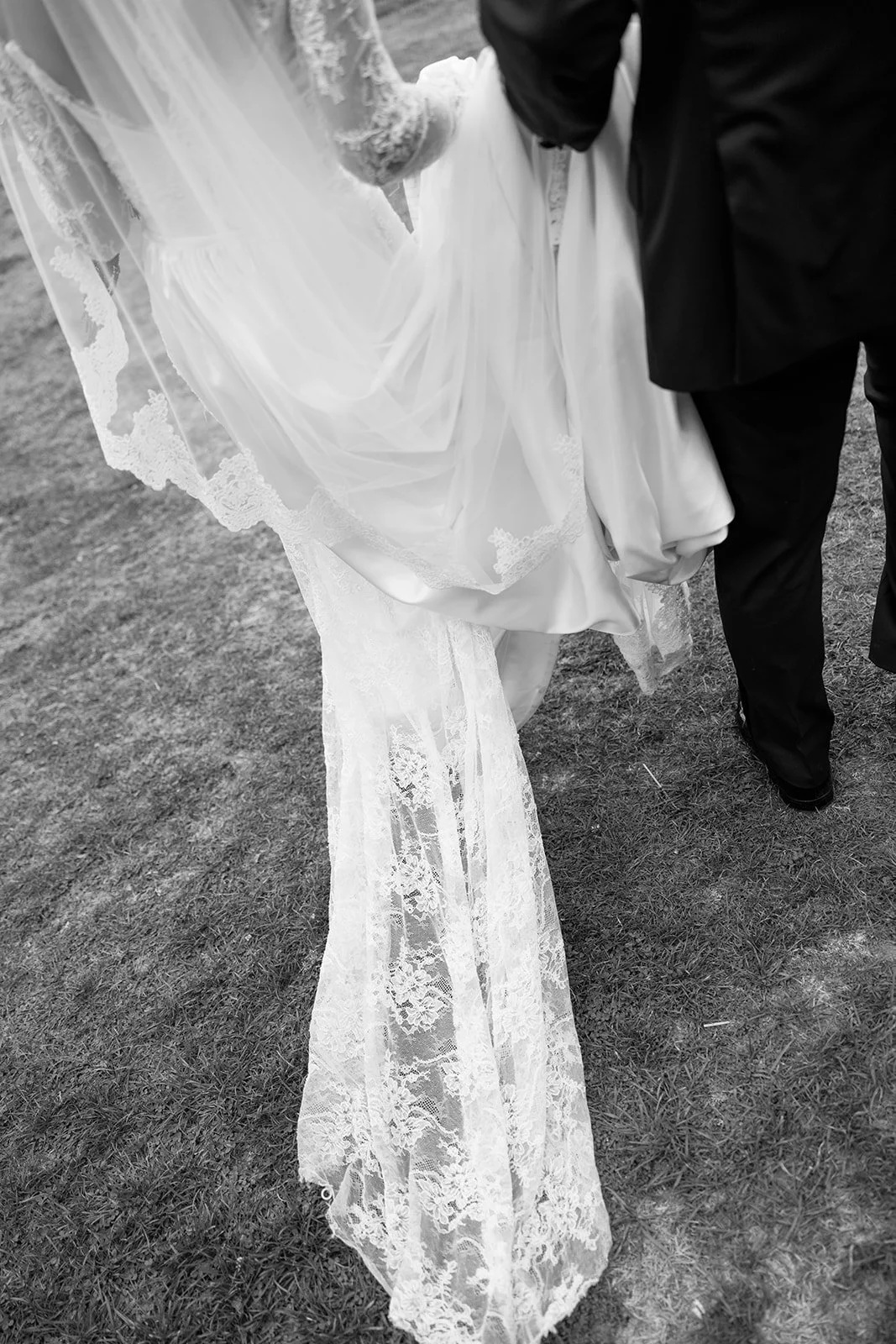 A bride being lifted by a groom during a wedding, showing the bride's lace wedding dress and veil, and the groom's suit.