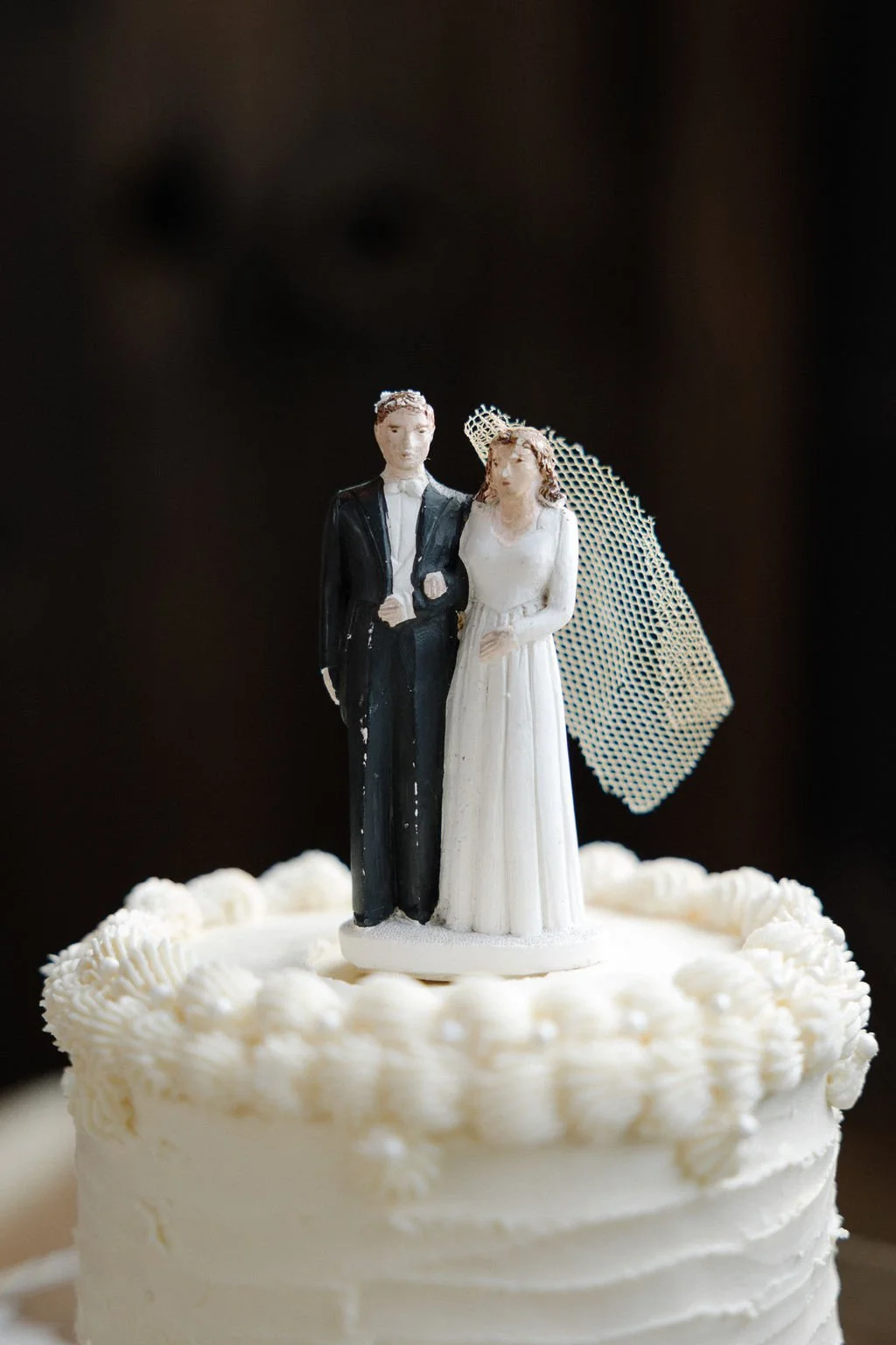 Wedding cake topper with a bride and groom figurine on a white frosted cake with piped decorative border.