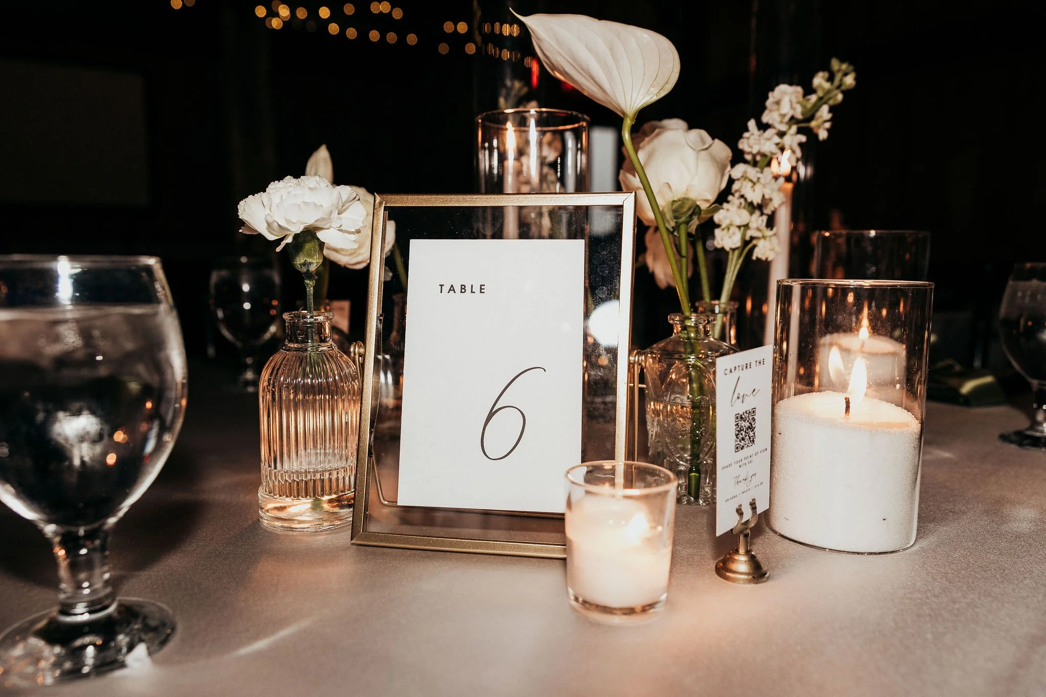 Decorative table setting with candles, flowers, and table number card at an event.