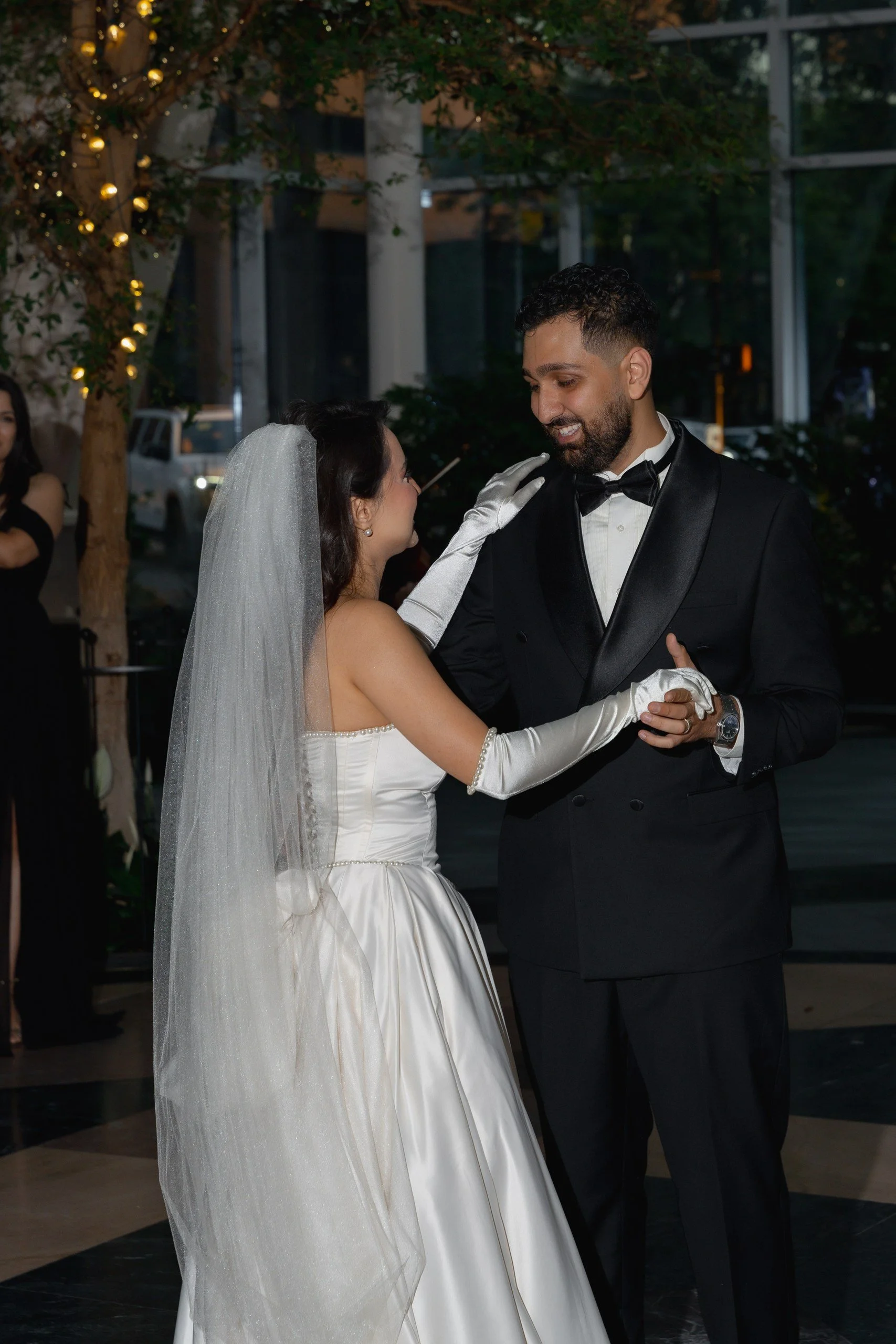 A bride and groom dancing at their wedding reception. The bride is wearing a white wedding dress and veil, and the groom is in a black tuxedo. They are smiling and holding each other as they dance.