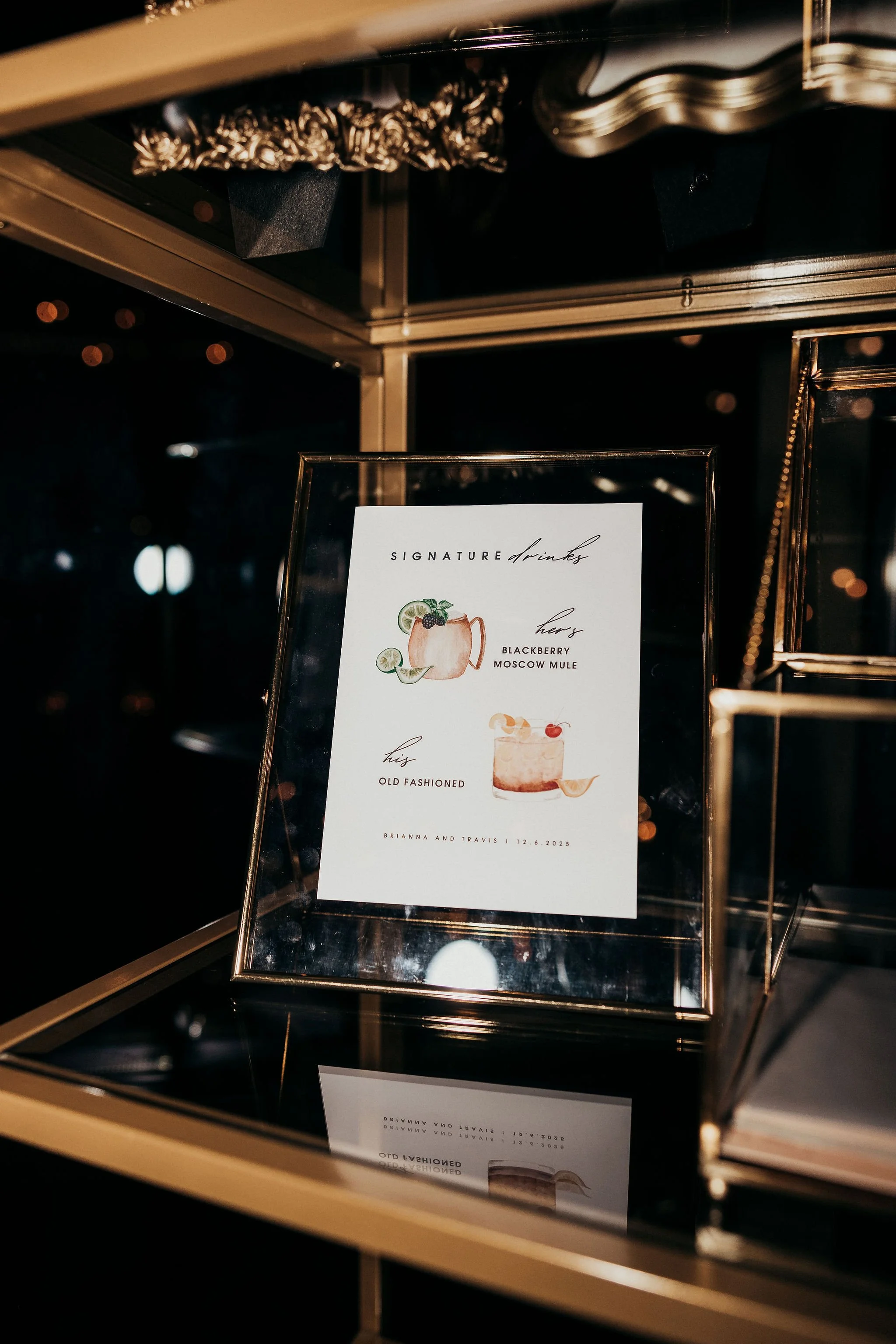 Menu displaying signature drinks, including Blackberry Moscow Mule and Old Fashioned, on an elegant stand with a glass case around it.