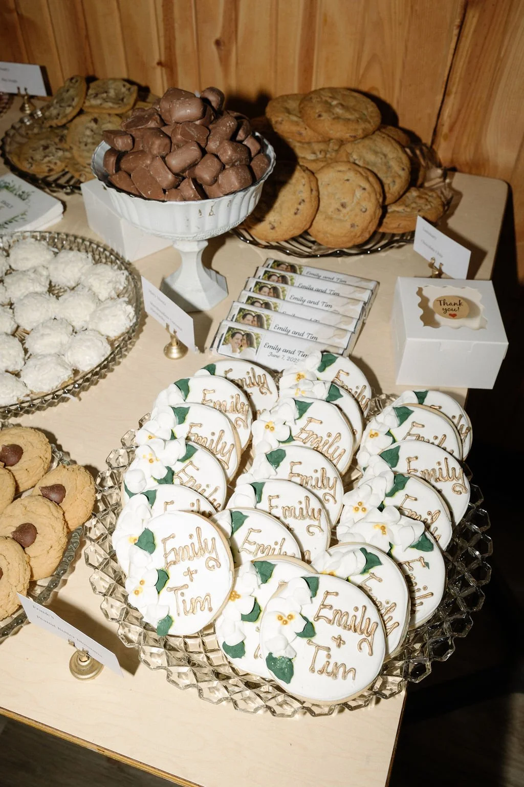 Assorted cookies and chocolates on a dessert table with personalized cookies reading 'Emily + Tim' and napkins with a wedding date.