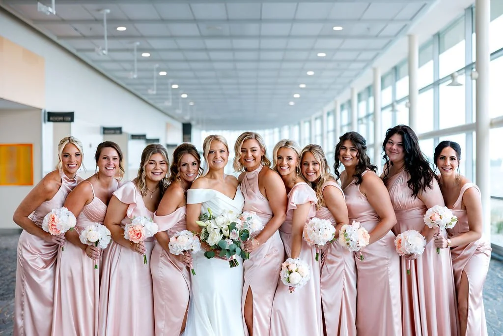 Bride in white gown with bridesmaids in pink dresses holding bouquets indoors.