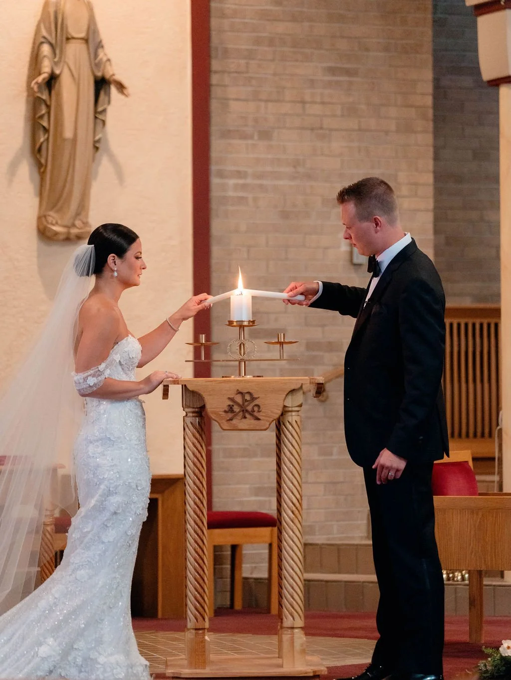 A bride and groom lighting a unity candle during their wedding ceremony in a church.