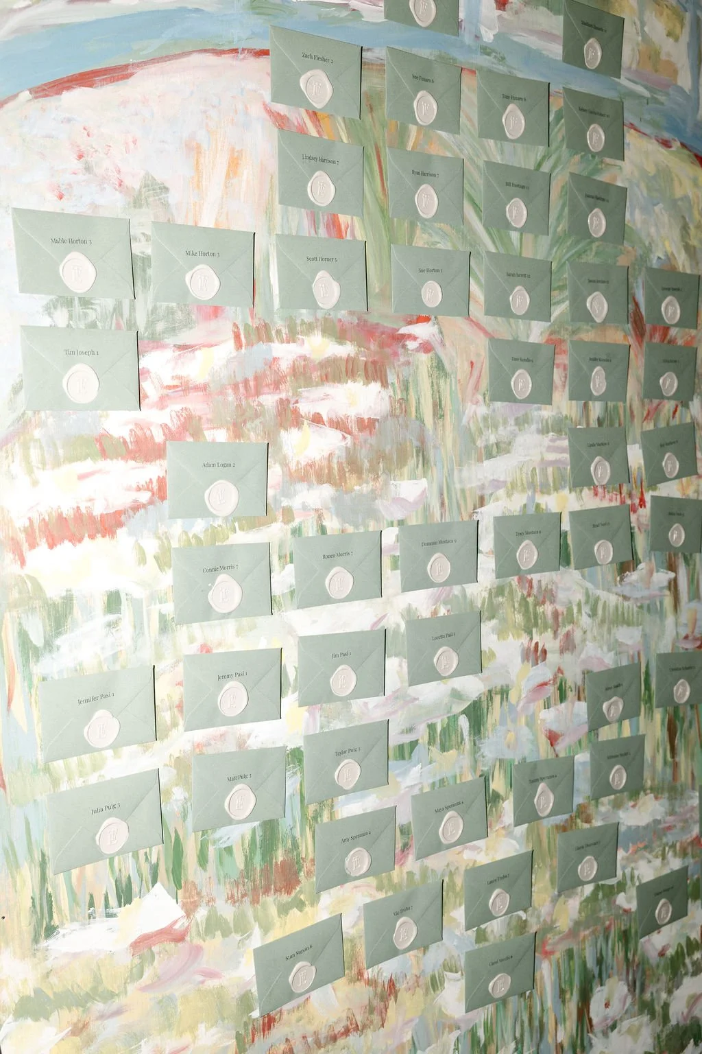Colorful abstract painting background with green paper envelopes, each sealed with white wax and labeled with names, arranged in rows