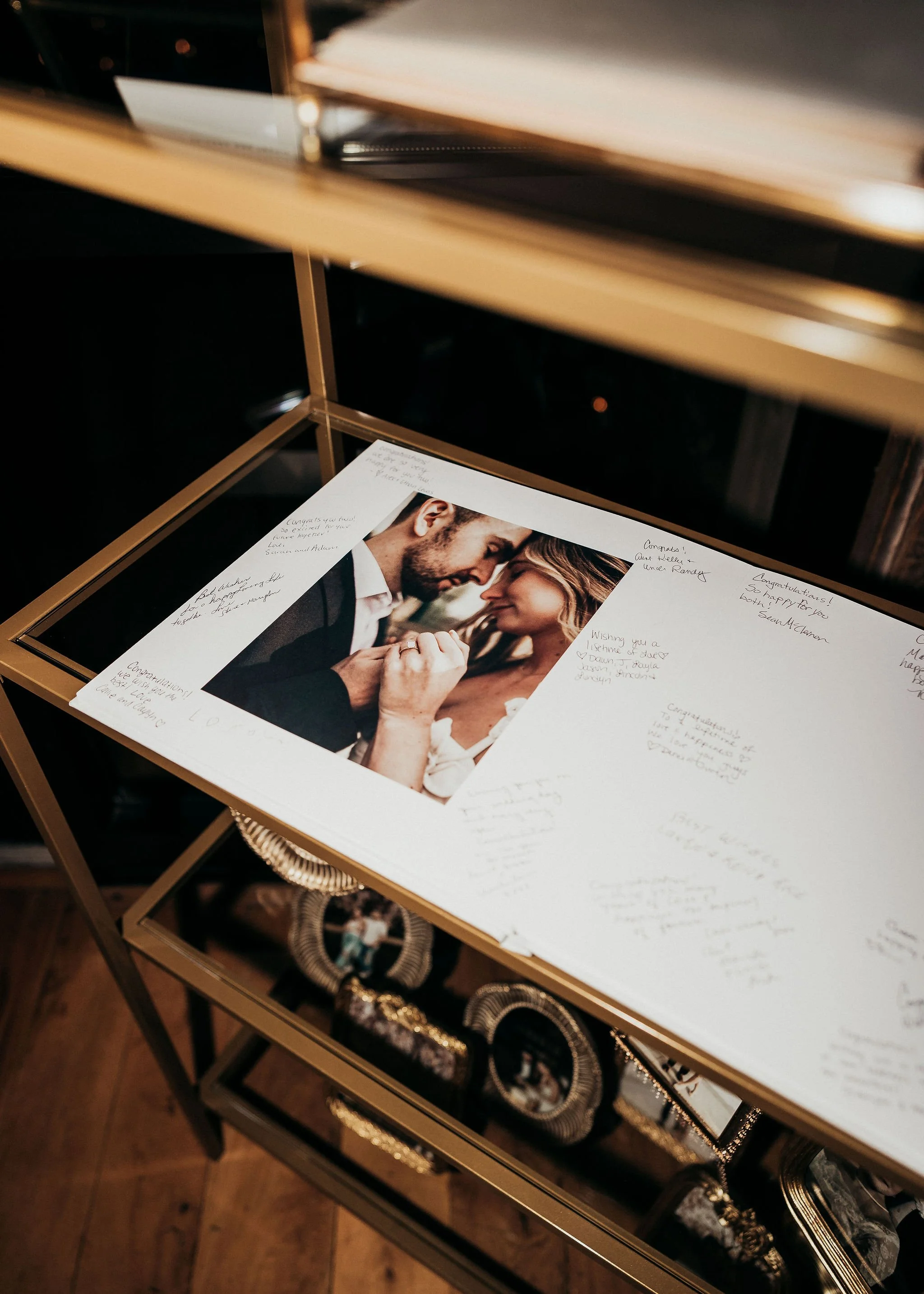 A glass display case with a photo of a couple on top, surrounded by handwritten notes and congratulations messages. The bottom shelves hold decorative items, jewelry, and accessories.