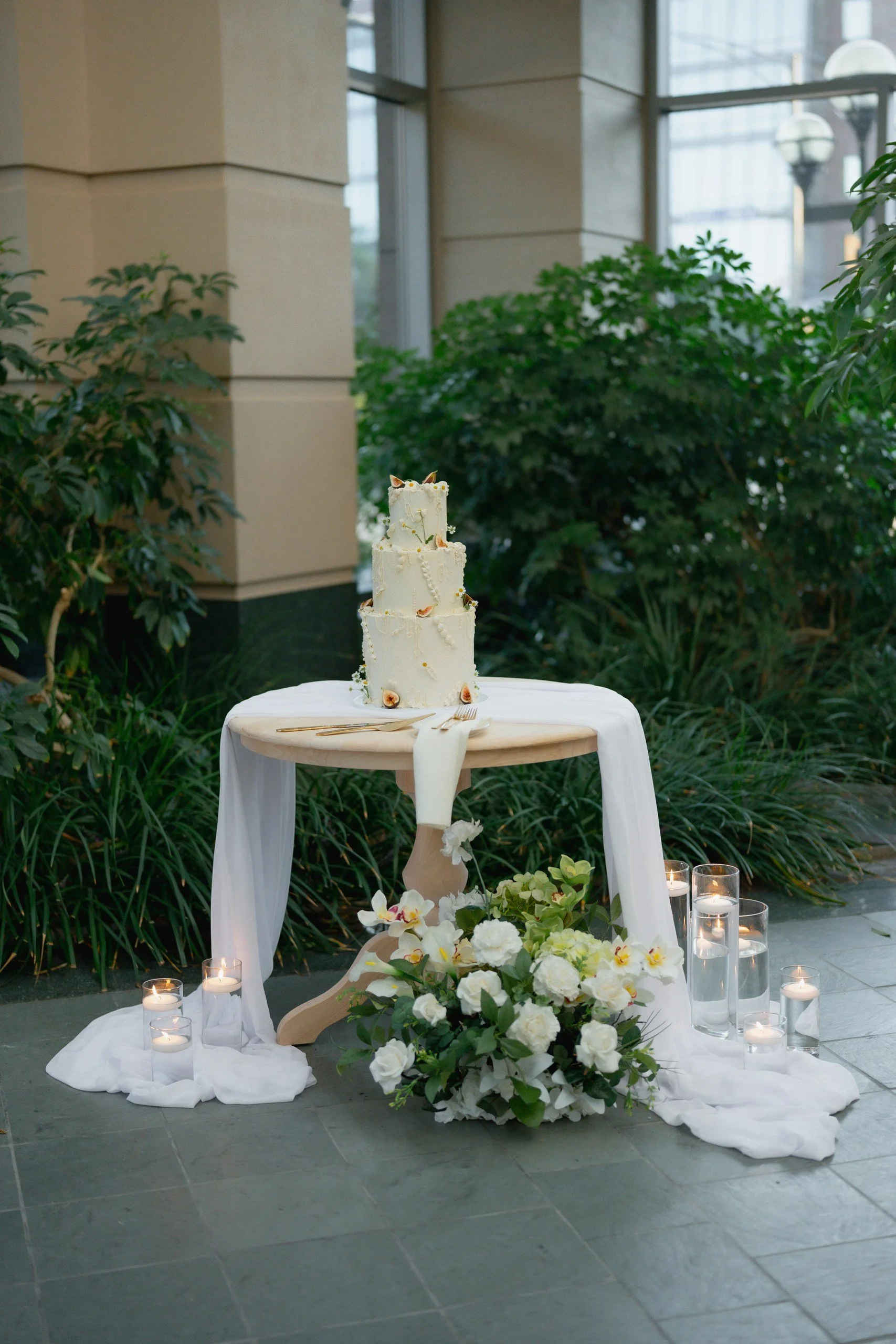 Elegant wedding cake on a table decorated with white linens and candlelit candles, surrounded by floral arrangements.