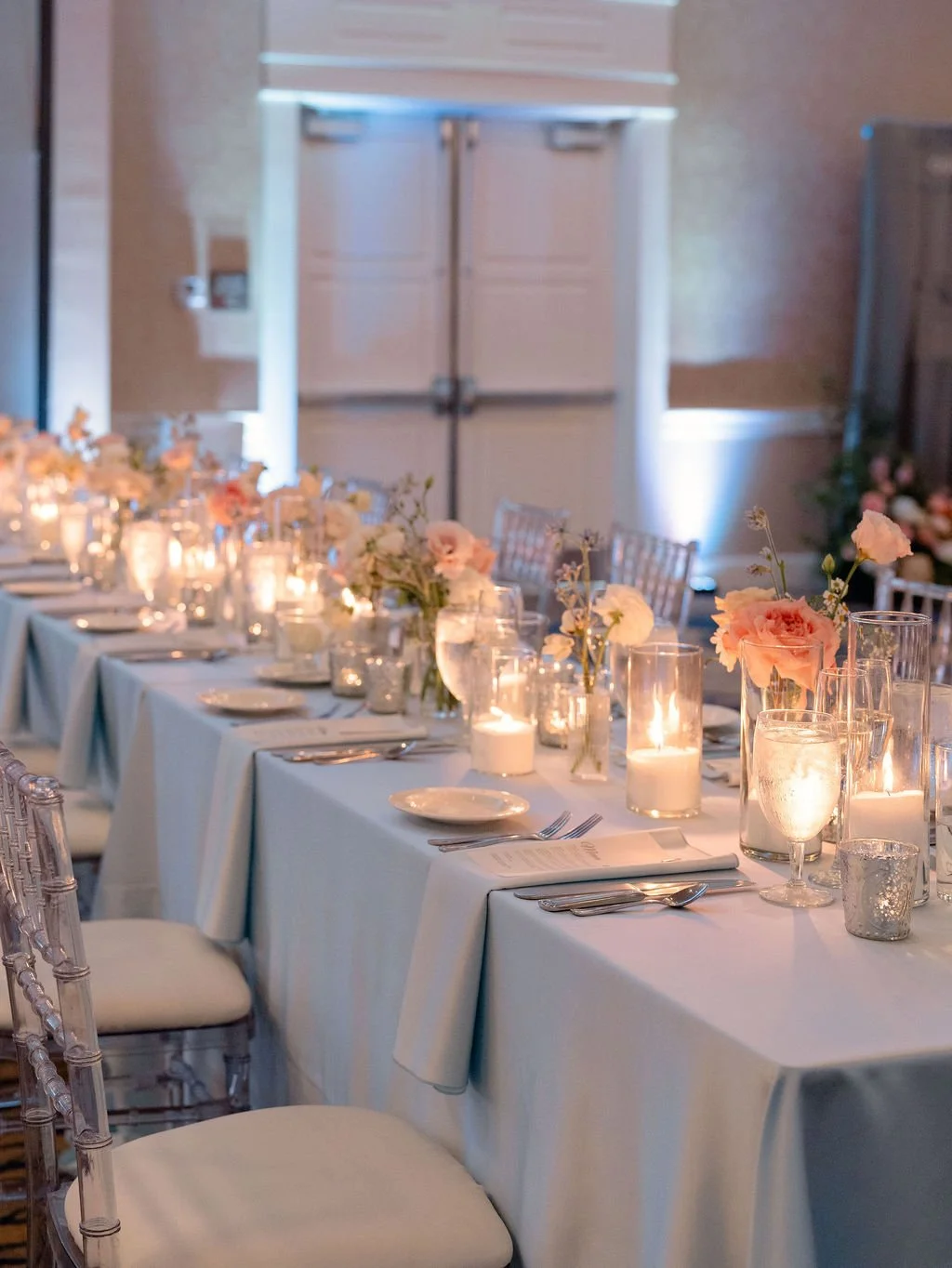 Elegant banquet table set with white tablecloths, floral centerpieces, candles, and place settings for a formal event or wedding reception.