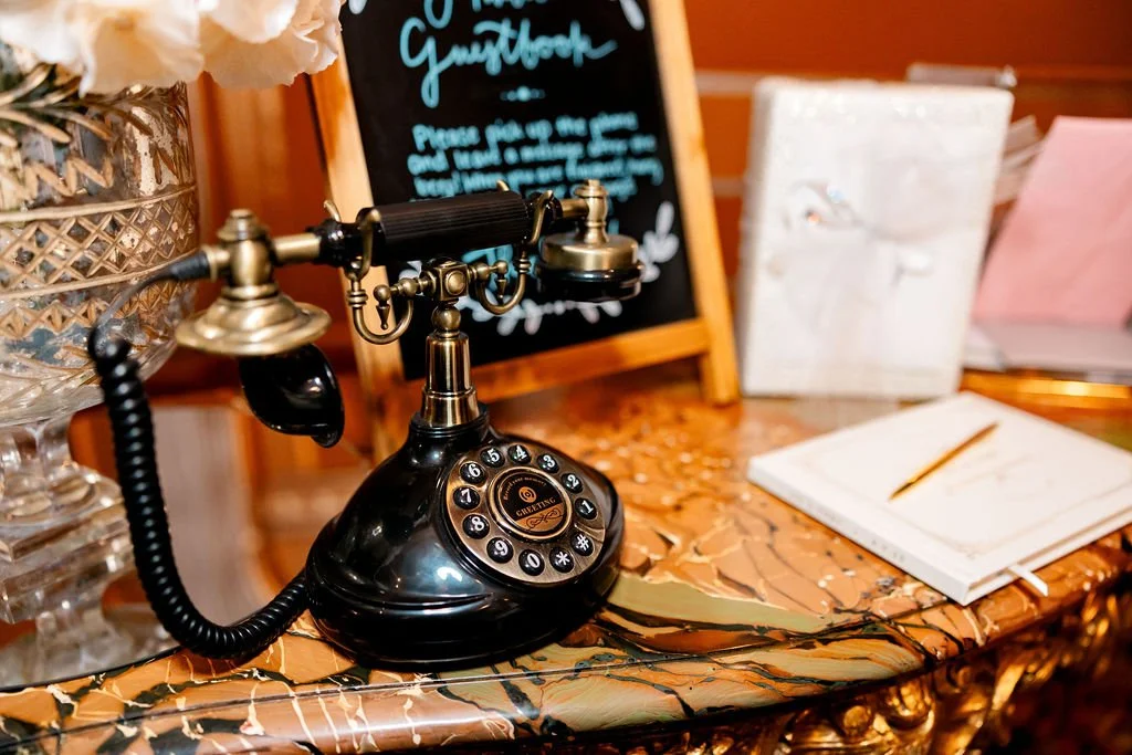 Vintage black rotary telephone on a marble table with notebooks and a chalkboard sign in the background.
