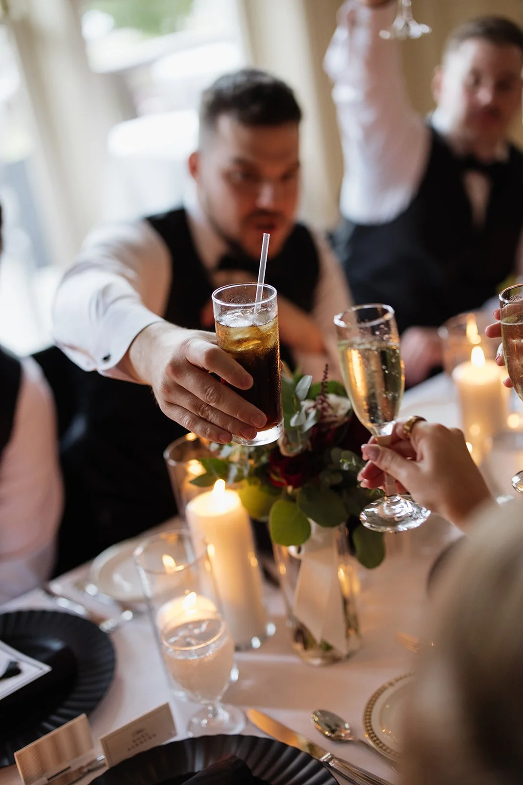 People at a dinner table raising glasses for a toast, surrounded by lit candles and floral decorations.