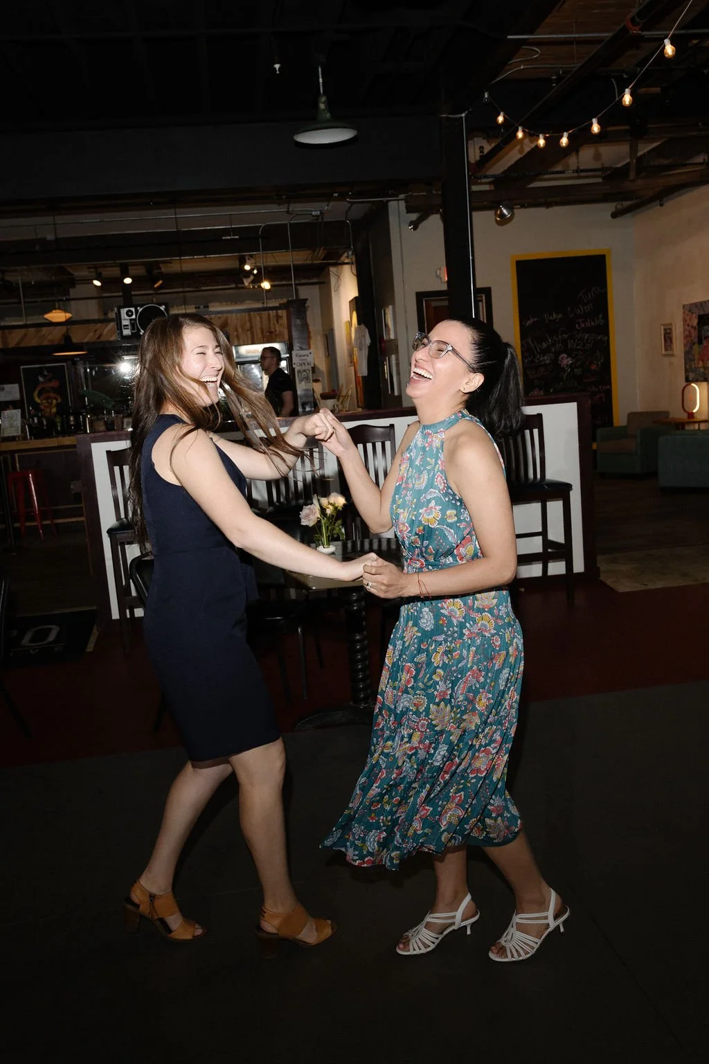 Two women laughing and dancing in a dimly lit restaurant or bar
