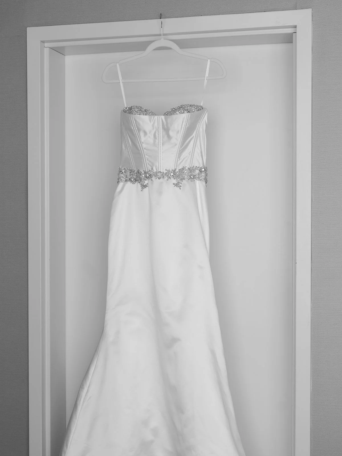 White wedding dress with beaded embellishments hanging on a white hanger in a closet.