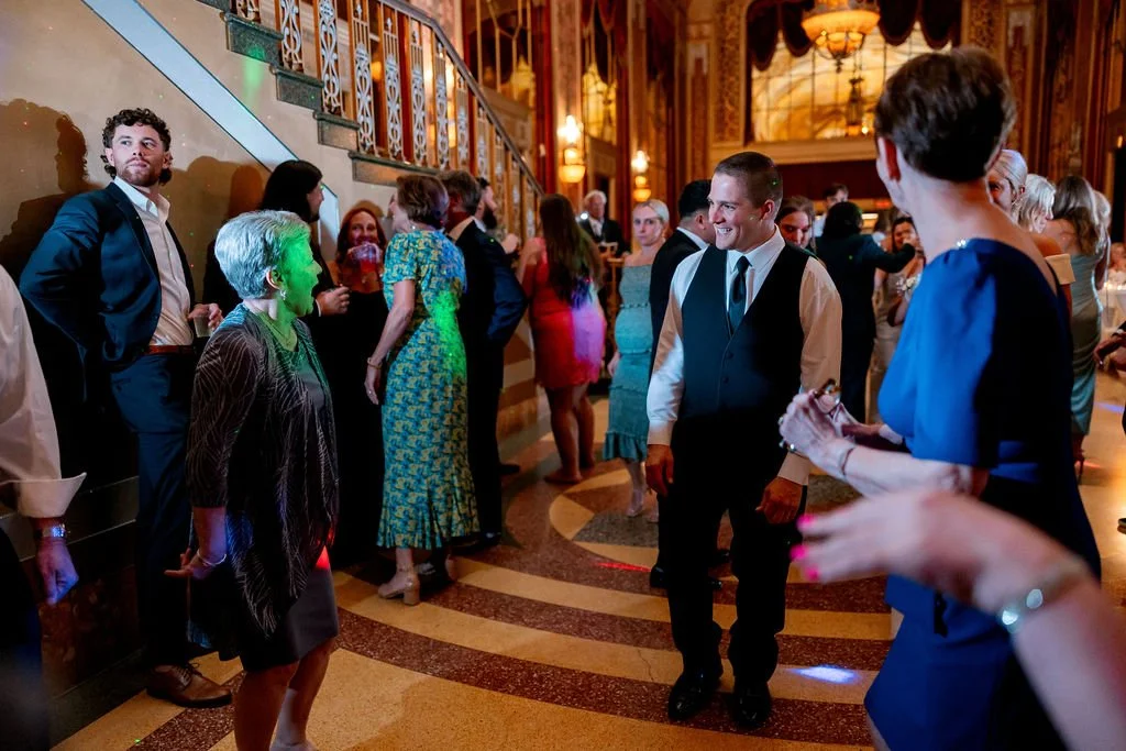 People socializing and dancing at an elegant indoor event with ornate decor and warm lighting.
