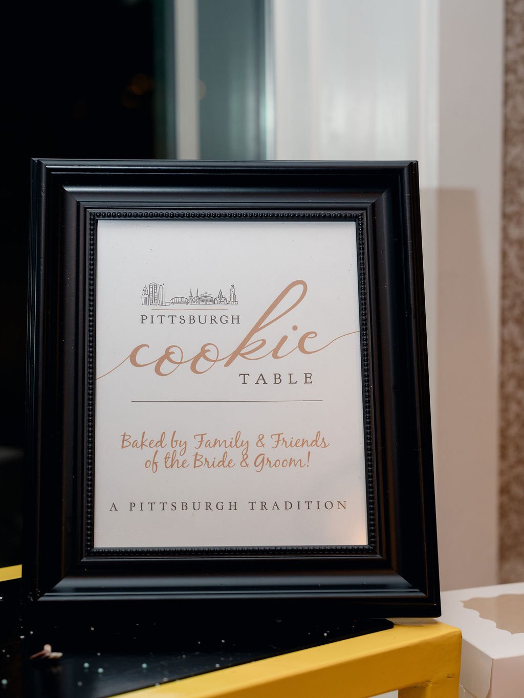 Sign for a Pittsburgh cookie table at a wedding, indicating it is baked by family and friends of the bride and groom, with a skyline illustration of Pittsburgh at the top.