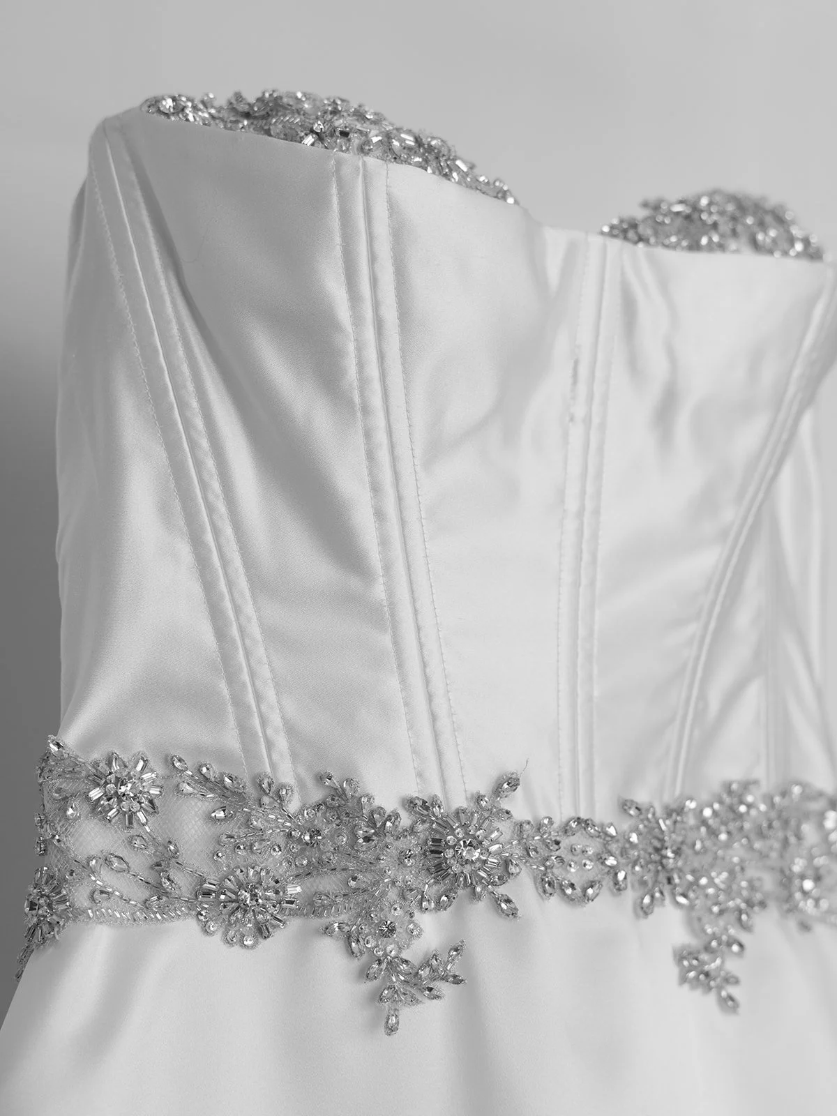 Close-up of a white satin wedding dress with intricate beaded floral embroidery around the waist and neckline.