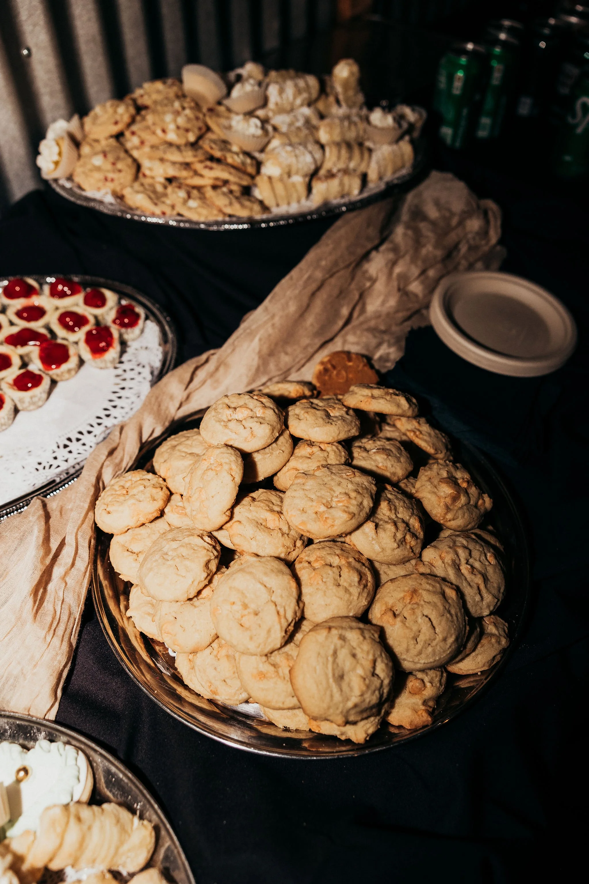 Large platter of chocolate chip cookies with a smaller tray of cupcakes topped with red fruit and white icing in the foreground.