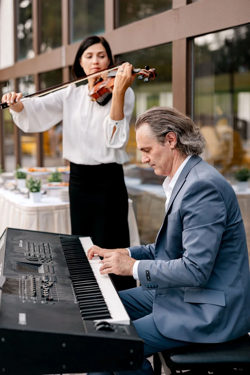 A woman playing the violin and a man playing the keyboard during a live performance.