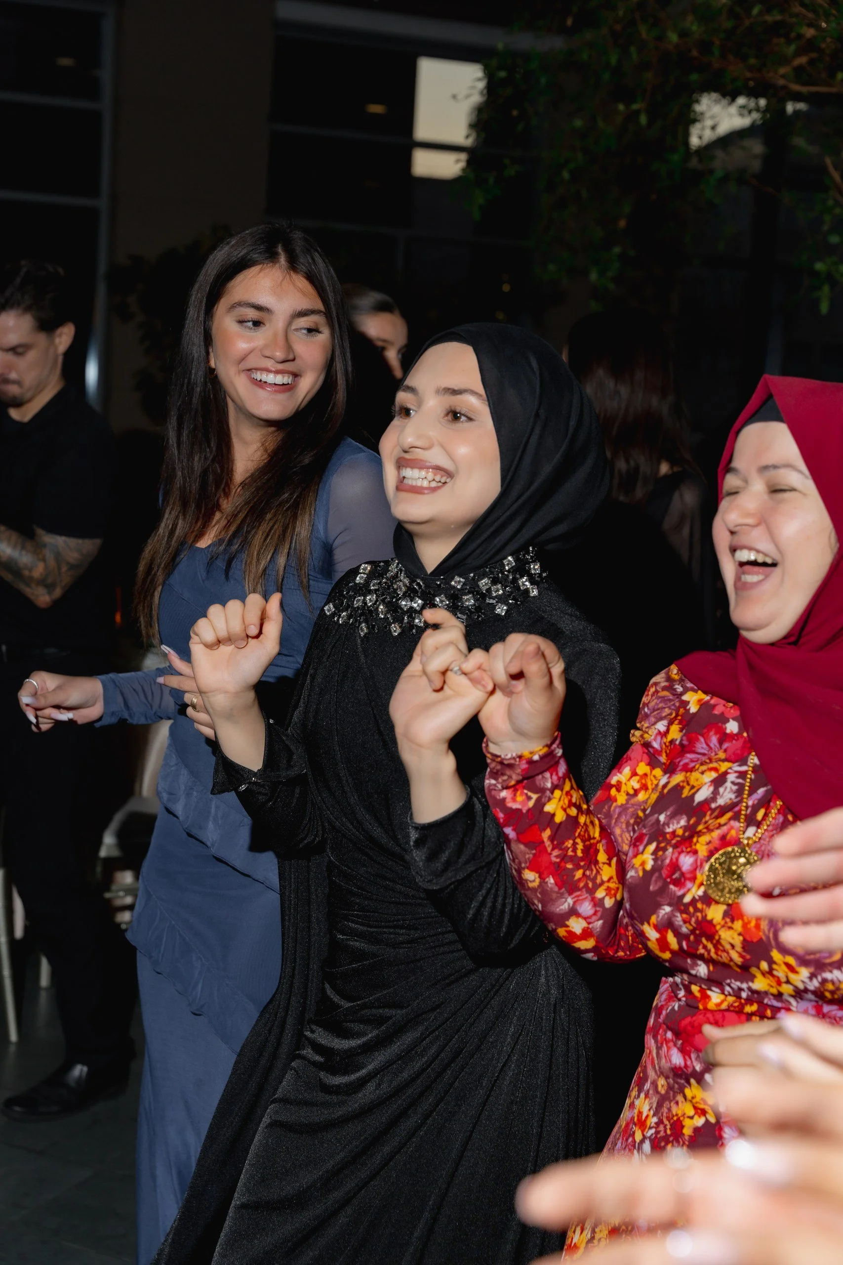 Three women smiling and holding hands together at a social event, smiling.