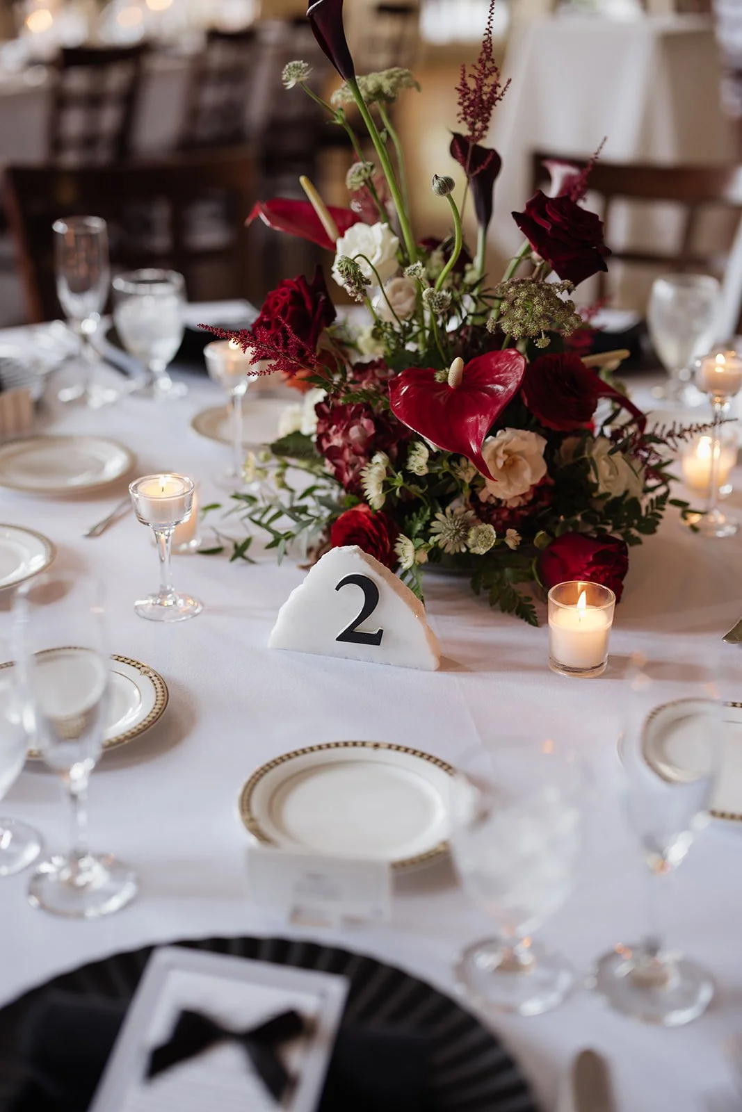 A table setting at a formal event with a floral centerpiece, candles, and a table number 2 card.