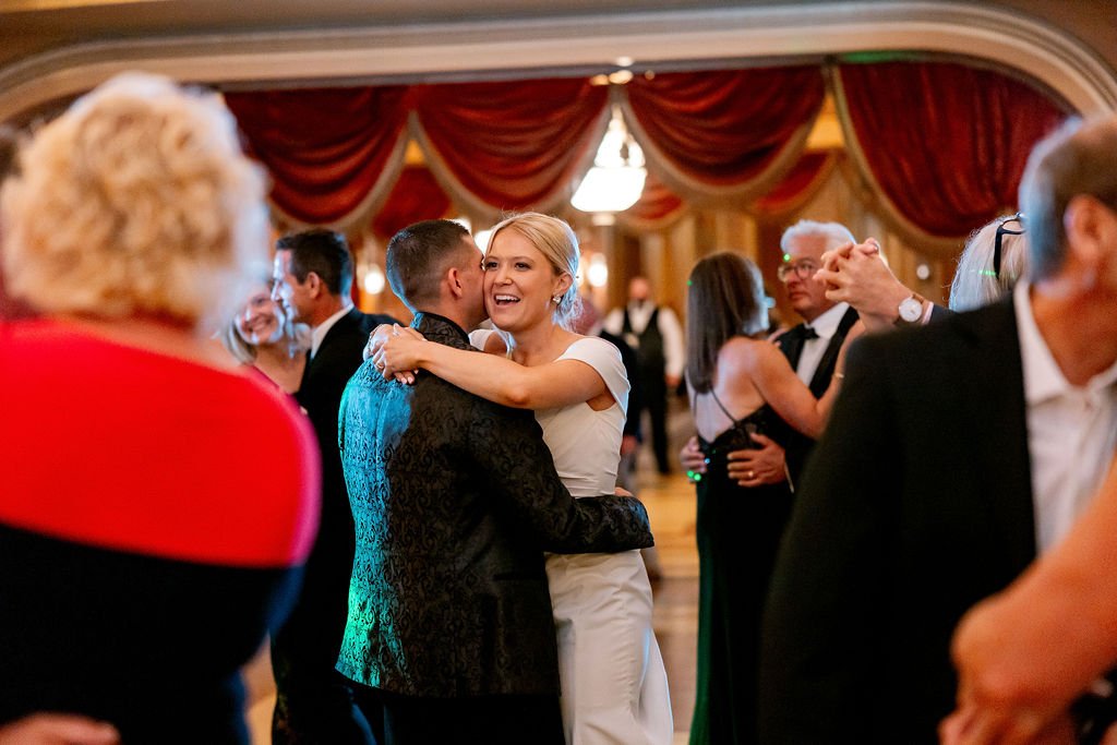 A bride and groom share a dance at their wedding reception, surrounded by guests.