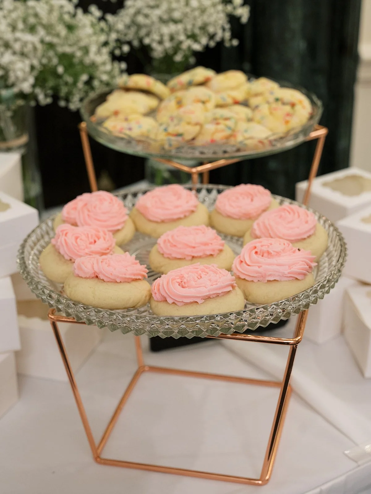Plate of sugar cookies with pink frosting on a glass cake stand