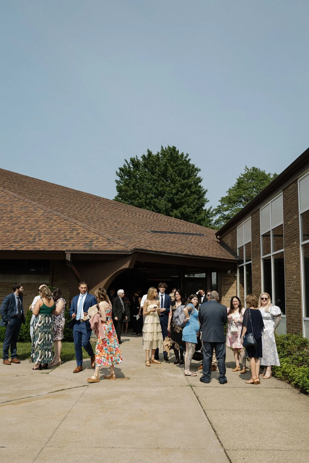 Group of people gathered outside a building, dressed in formal and semi-formal attire, likely attending an event or celebration.
