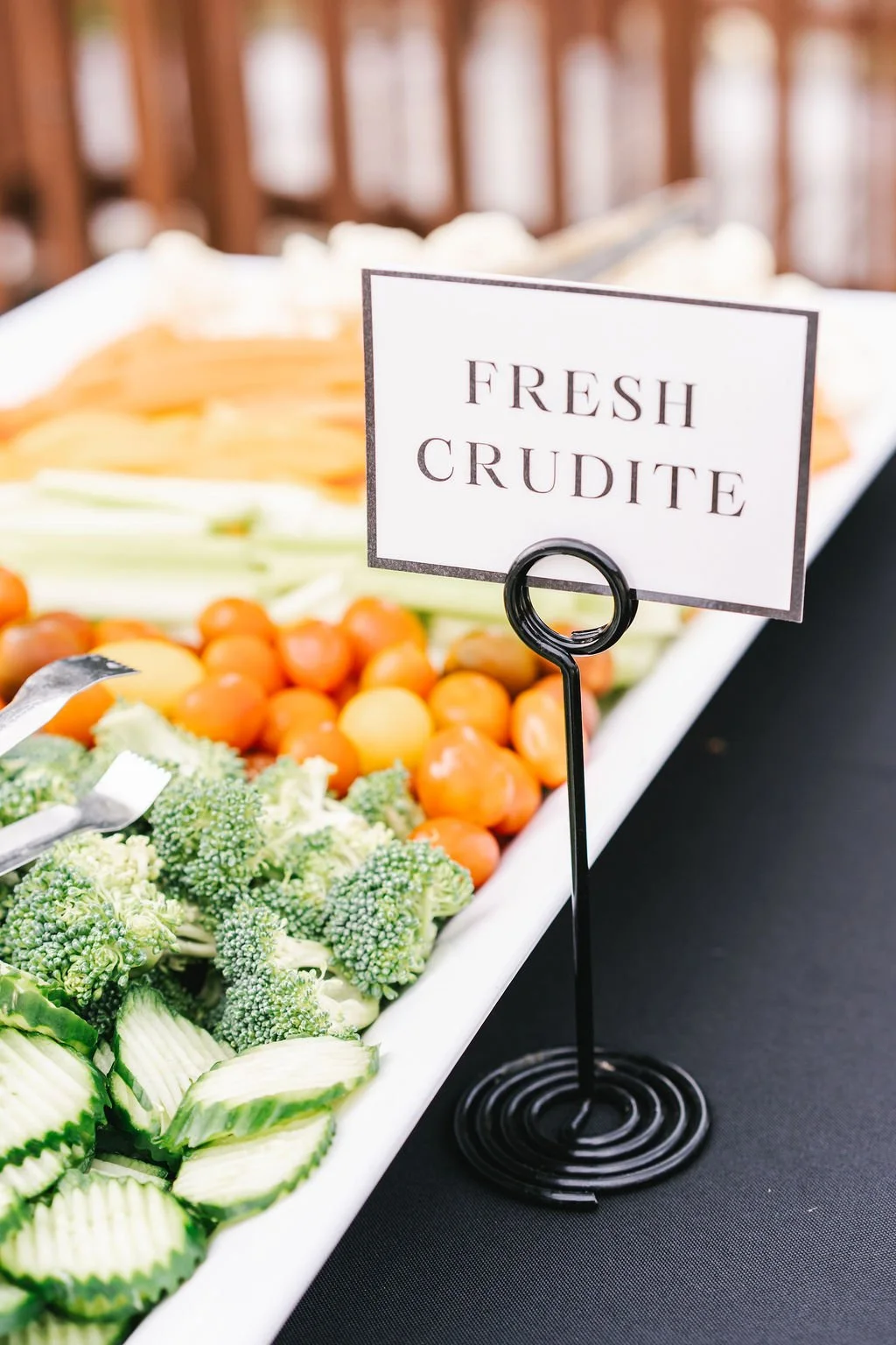 Platters of fresh vegetables, including broccoli, cherry tomatoes, and sliced cucumbers, with a sign reading 'Fresh Crudité' in the foreground.