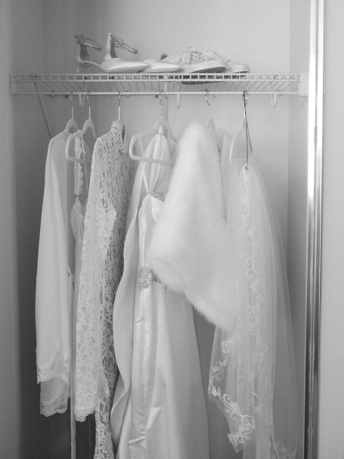 Inside a closet with wedding dresses and accessories, including a veil, hanging on hangers.