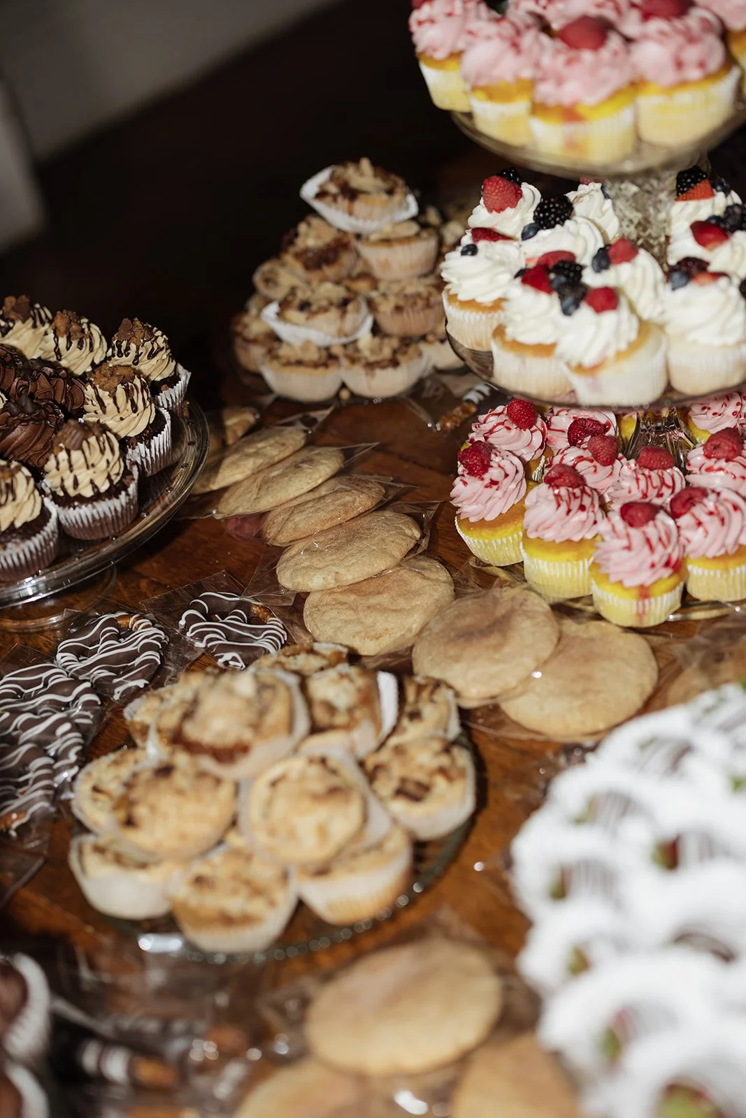 A variety of desserts including cupcakes with whipped cream and berries, cookies, oatmeal cups, and small pastry bites are arranged on a table for a dessert buffet.
