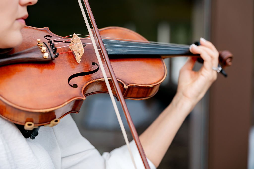 Close-up of a person playing a violin outdoors, focusing on the violin and their hand on the fingerboard.