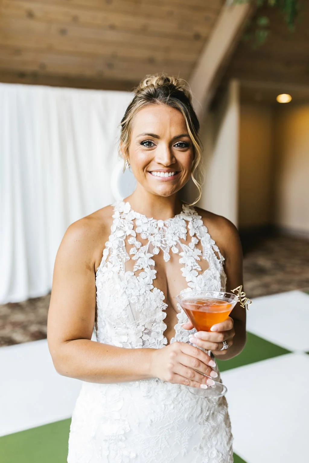 A woman in a white lace dress holding a cocktail glass at a wedding reception.